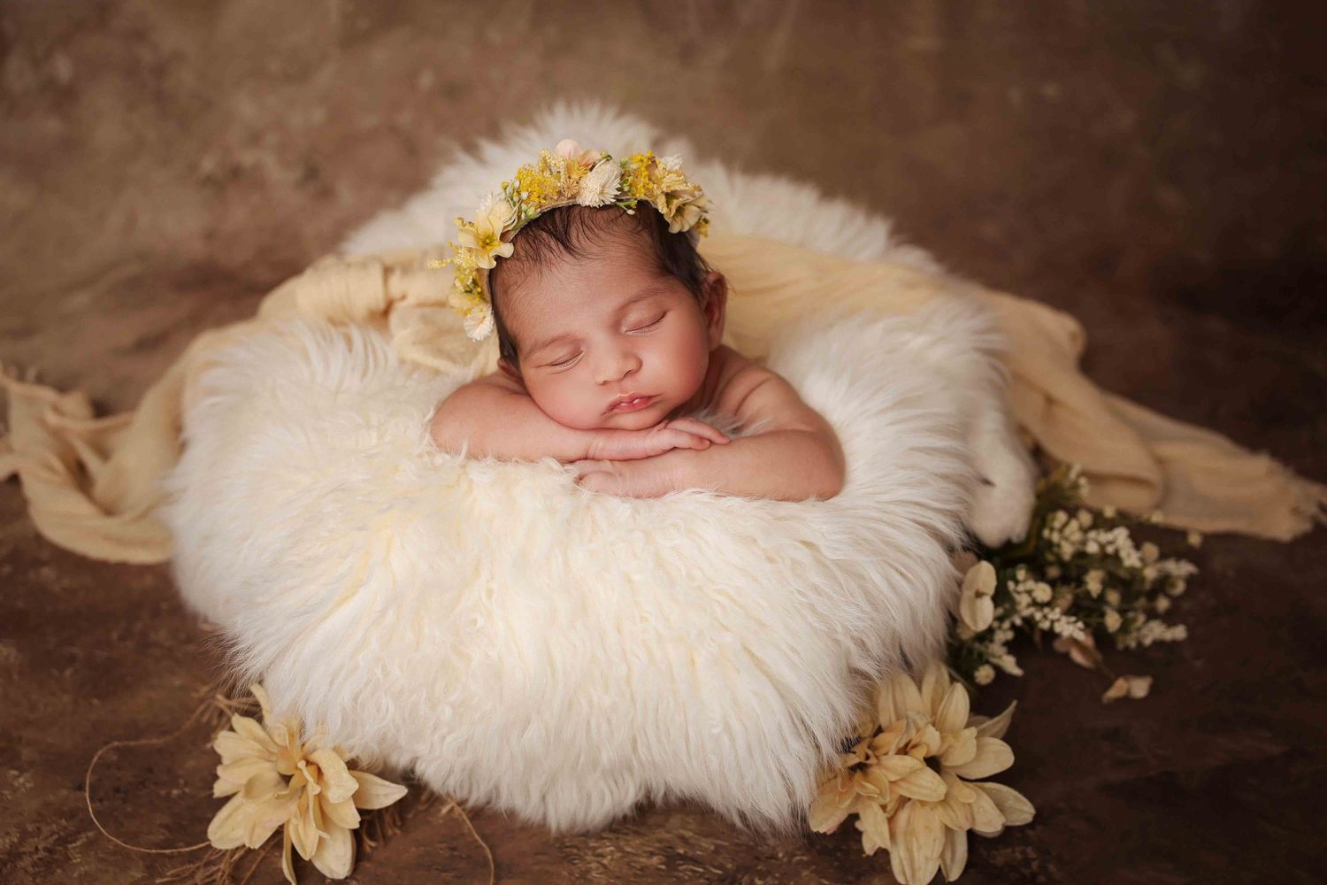 Sleeping newborn baby wearing a yellow flower crown rests on a soft cream fur rug surrounded by delicate blooms in a newborn photoshoot.
