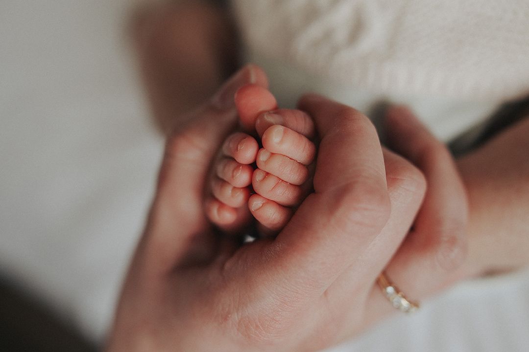 Close-up of a mother's hands gently cradling a newborn baby's tiny curled fingers, symbolizing love, family and new life.