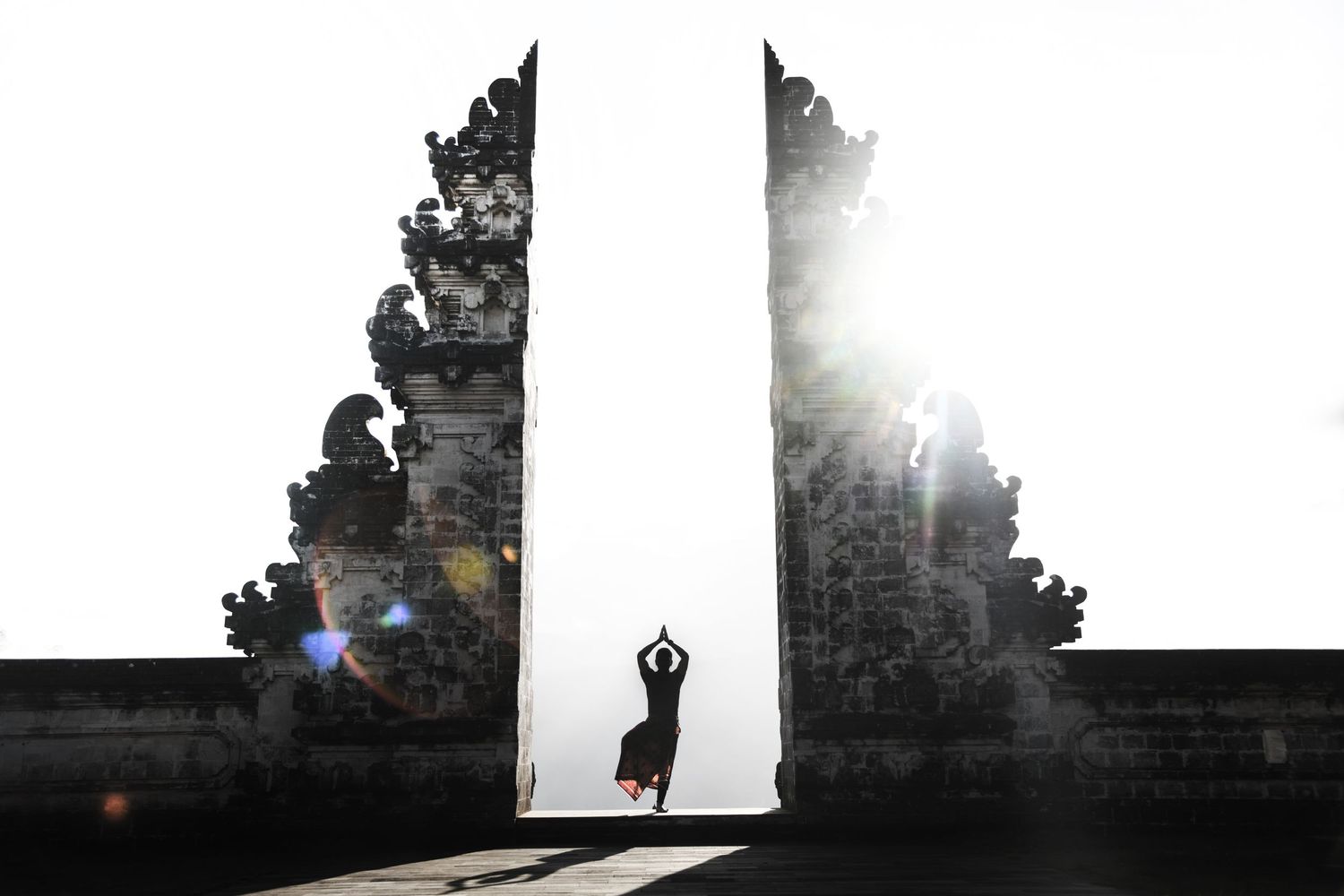 A person standing doing yoga silhouetted between the walls of an Indonesian temple
