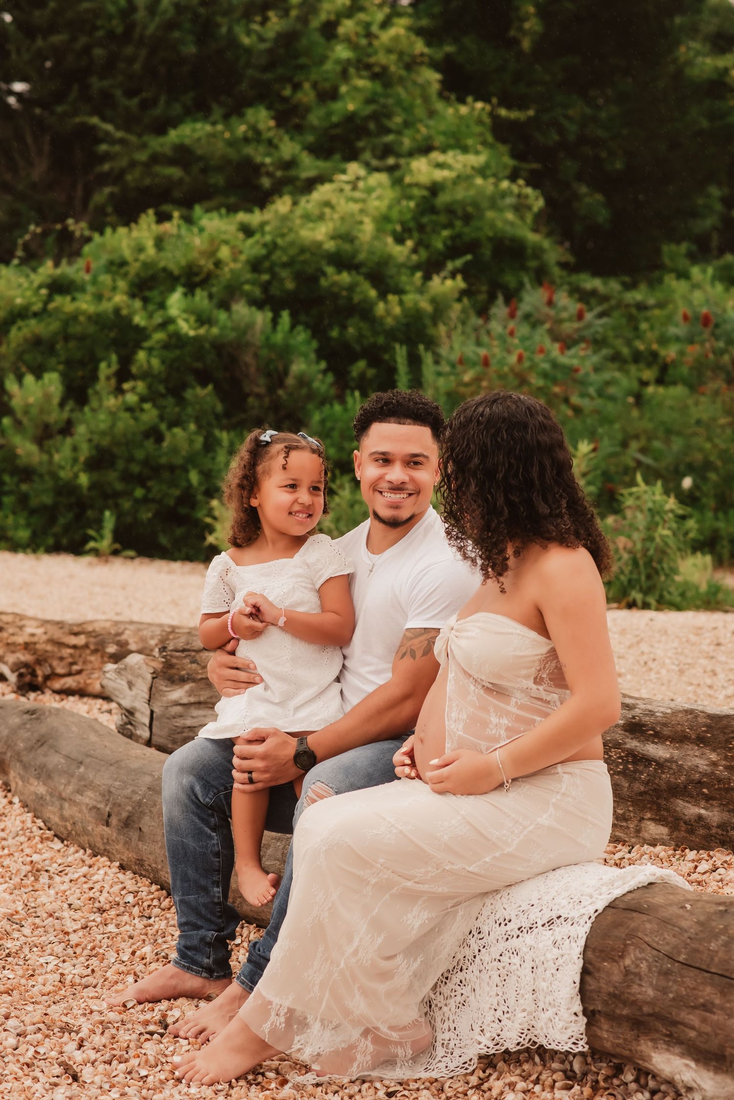 A family sits together on a rustic log bench outdoors surrounded by lush greenery in a natural setting.