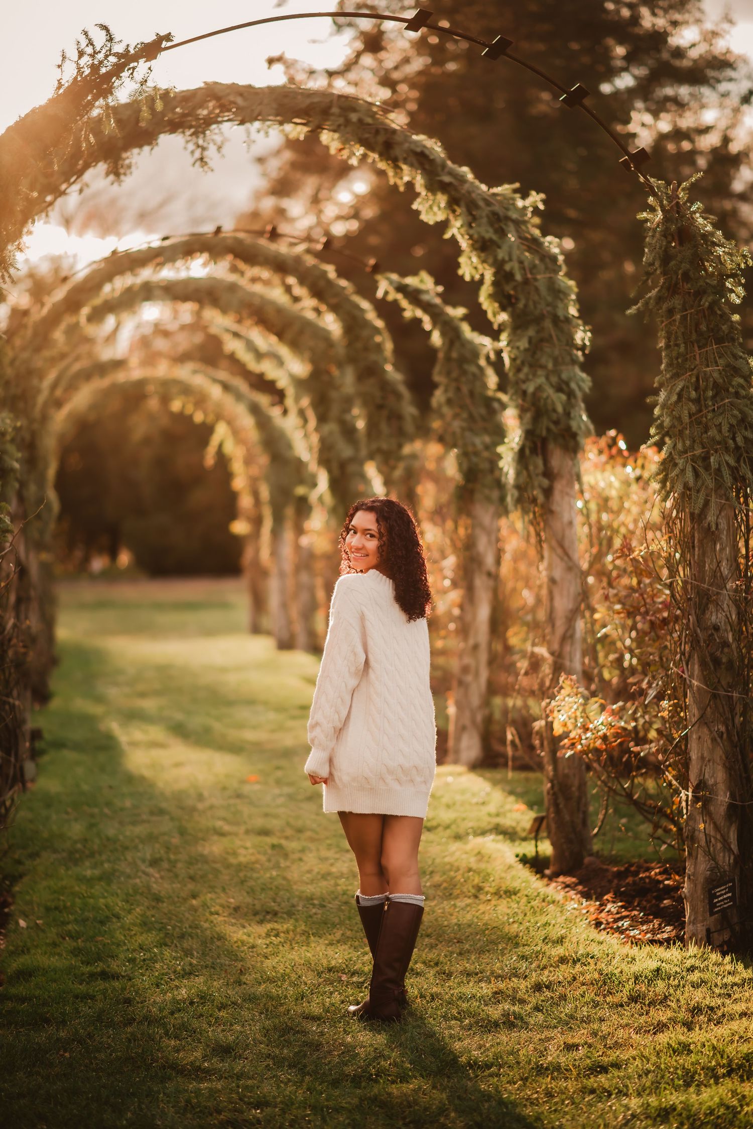 A dreamy autumn photoshoot in a garden arbor with golden sunlight filtering through the arches and trees.