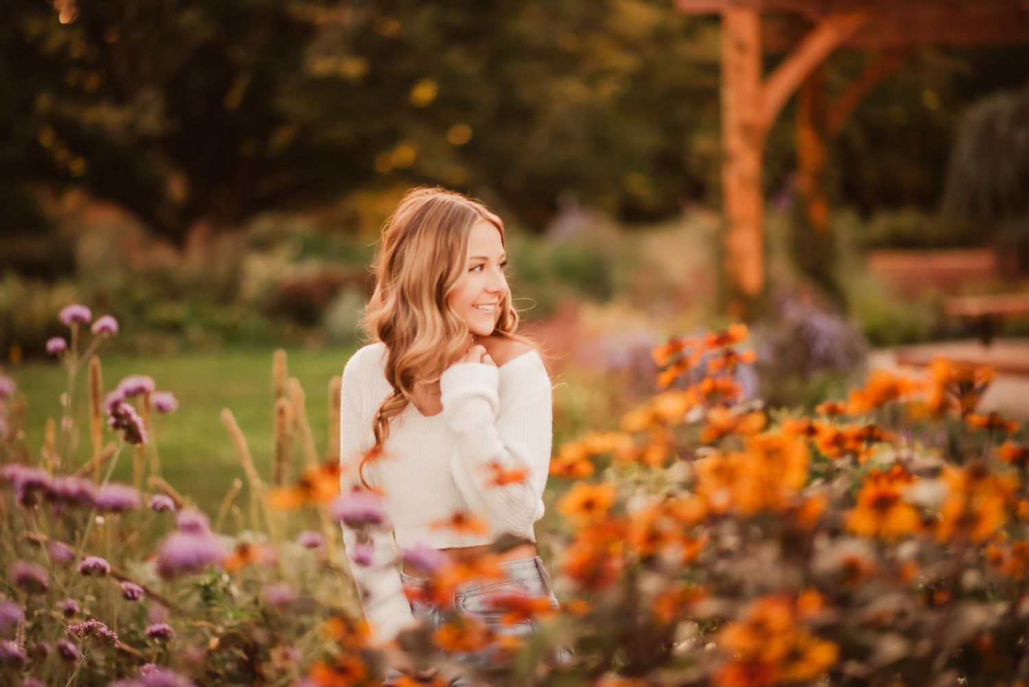A person sits among vibrant orange and purple flowers in a garden during golden hour sunset.