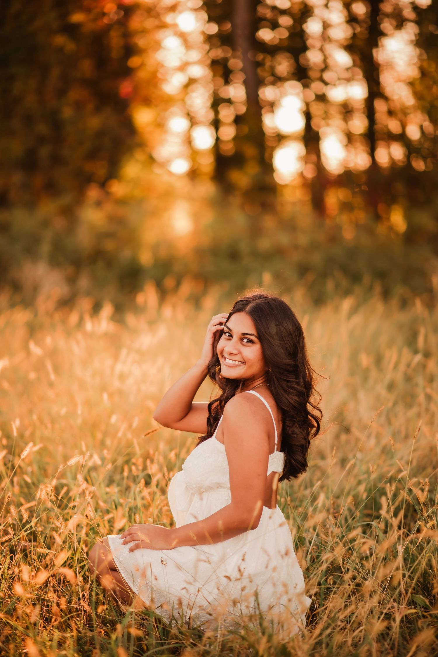 A woman in a white dress lies in golden grass during sunset creating a dreamy outdoor portrait series.