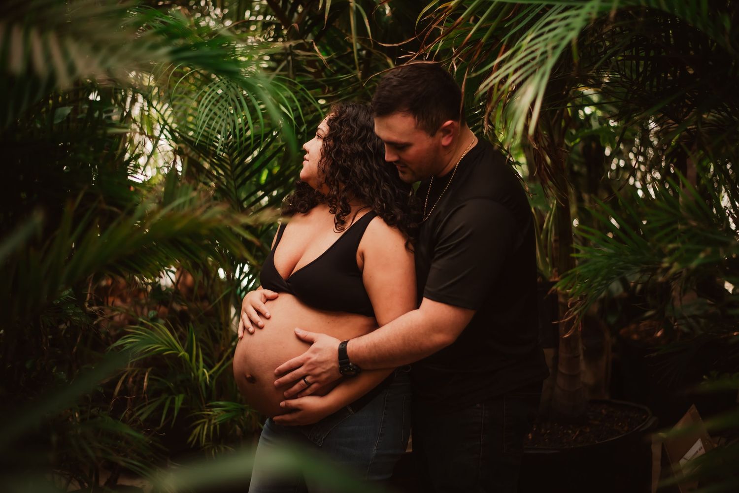 Romantic couple embraces intimately in a lush tropical garden setting with dramatic lighting and palm fronds.