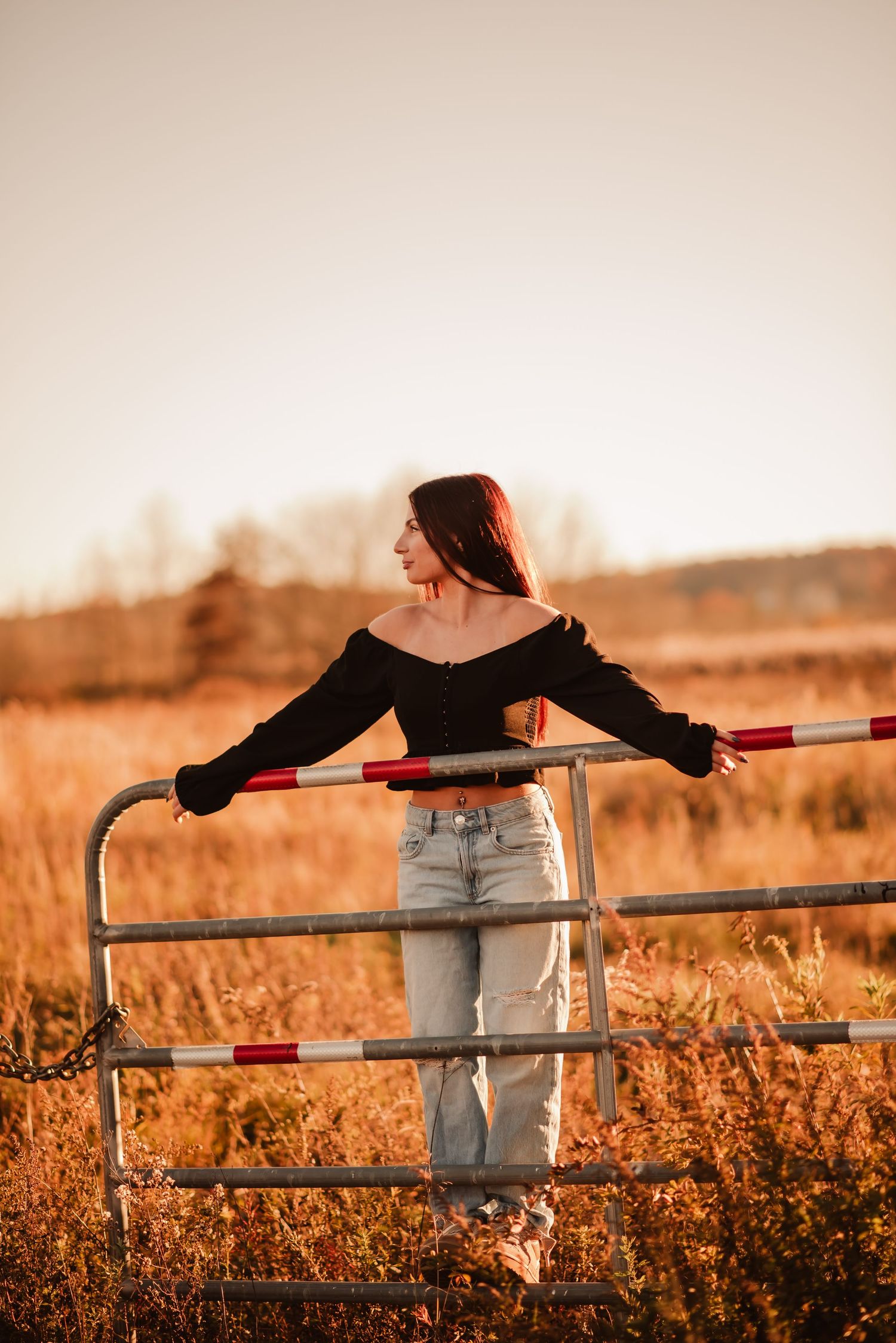 Person in jeans leans against rustic wooden fence at sunset in golden field with warm autumn lighting.
