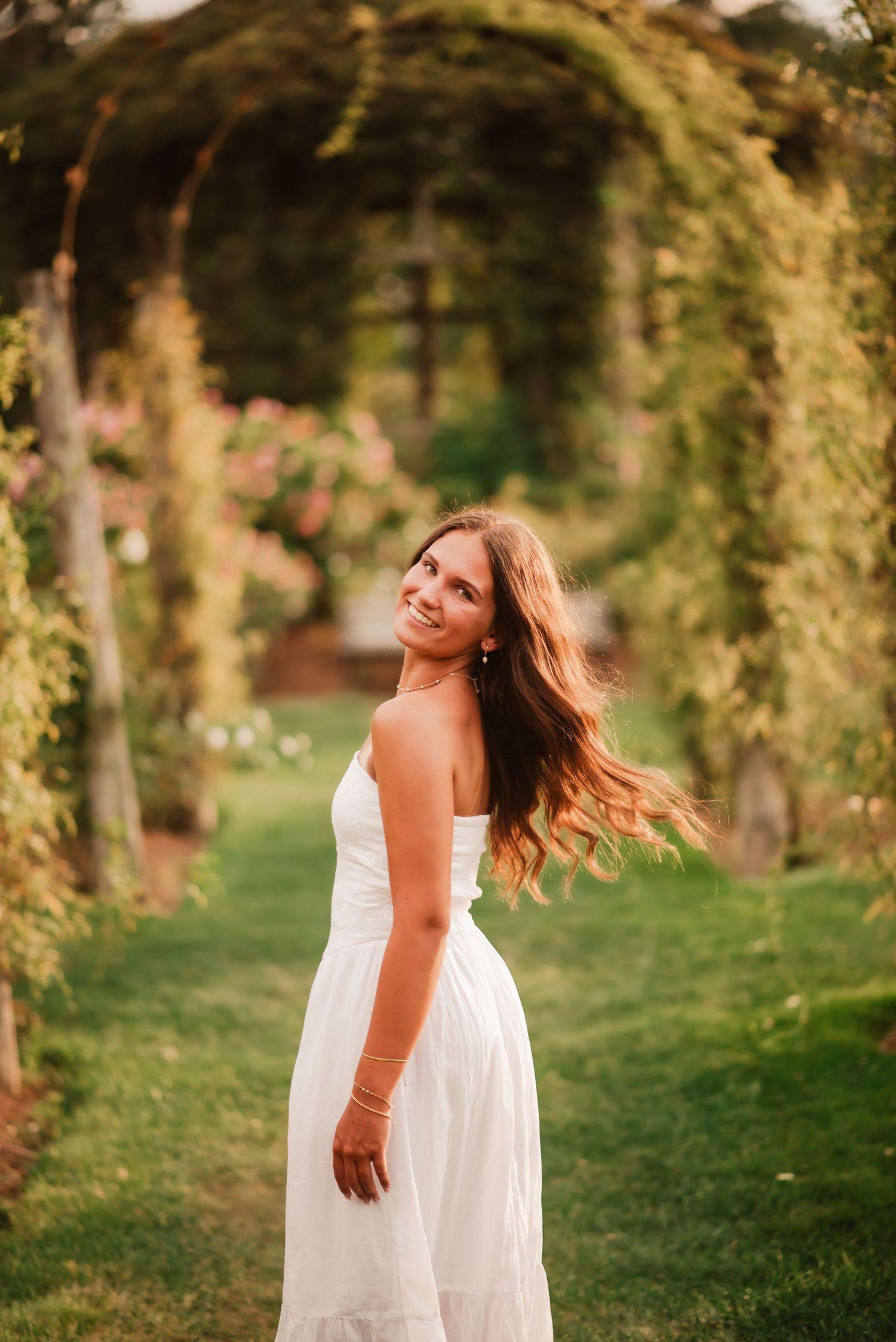 A person in a flowing white dress twirls joyfully in a sunlit forest setting during golden hour.