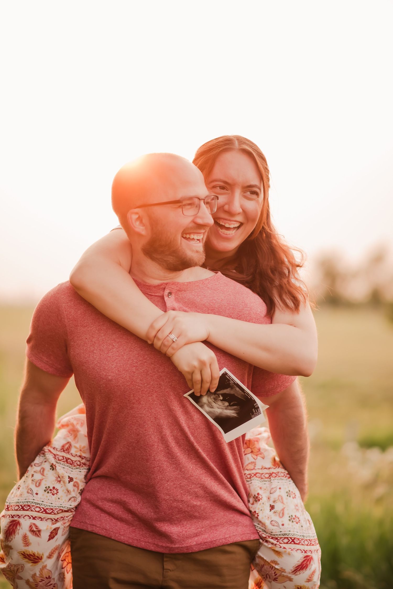 A couple embraces and laughs together in a field during golden hour sunset.