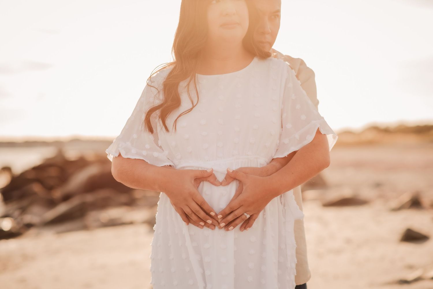 A couple in light flowy outfits share an intimate moment on a sandy beach at sunset.