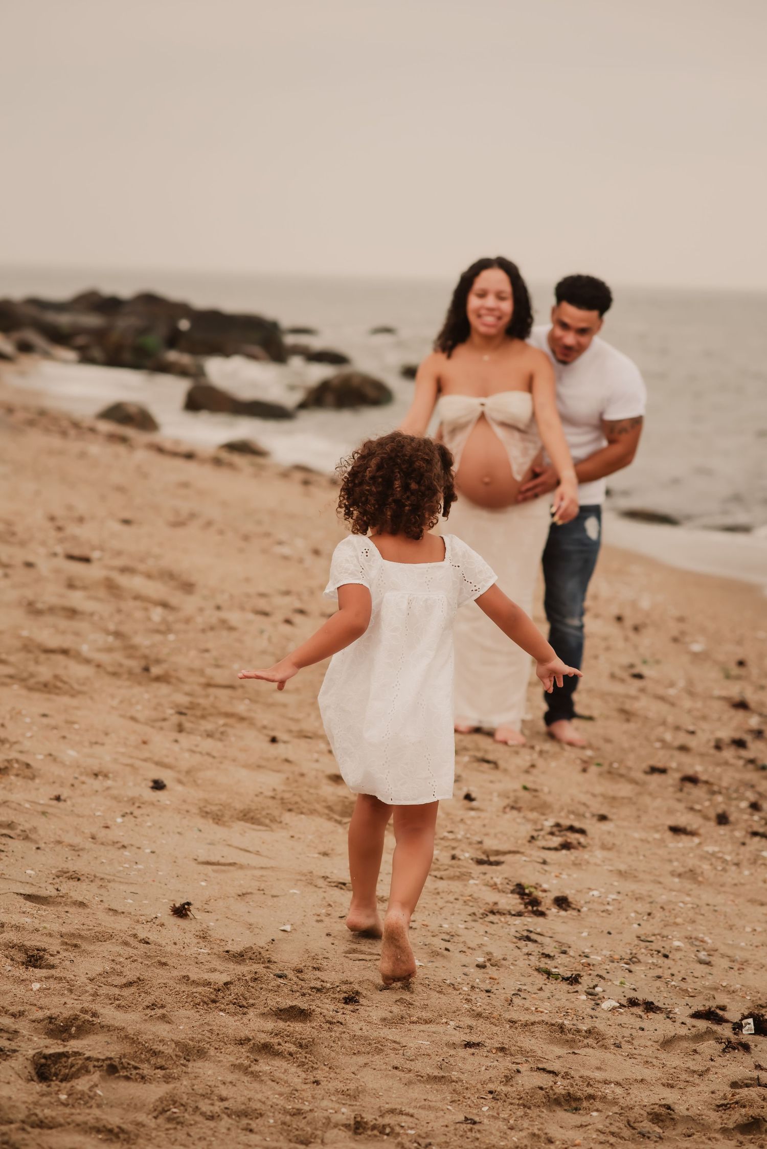 A family plays together on a sandy beach during sunset, creating joyful moments near the ocean waves.
