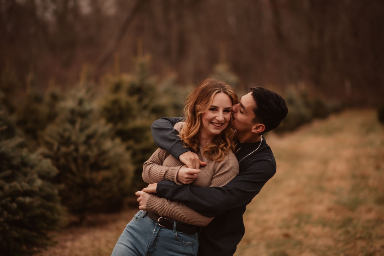 A romantic outdoor embrace between a couple on a hill during golden hour with evergreen trees in the background.