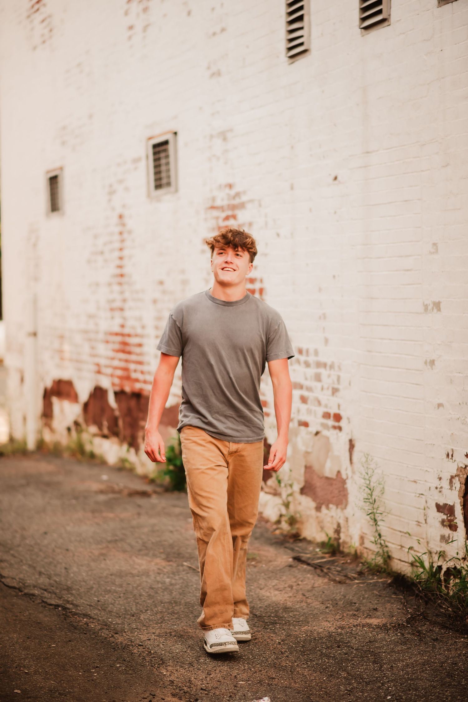 Three sequential photos showing a person walking and laughing along a white brick wall wearing khaki pants and gray shirt.