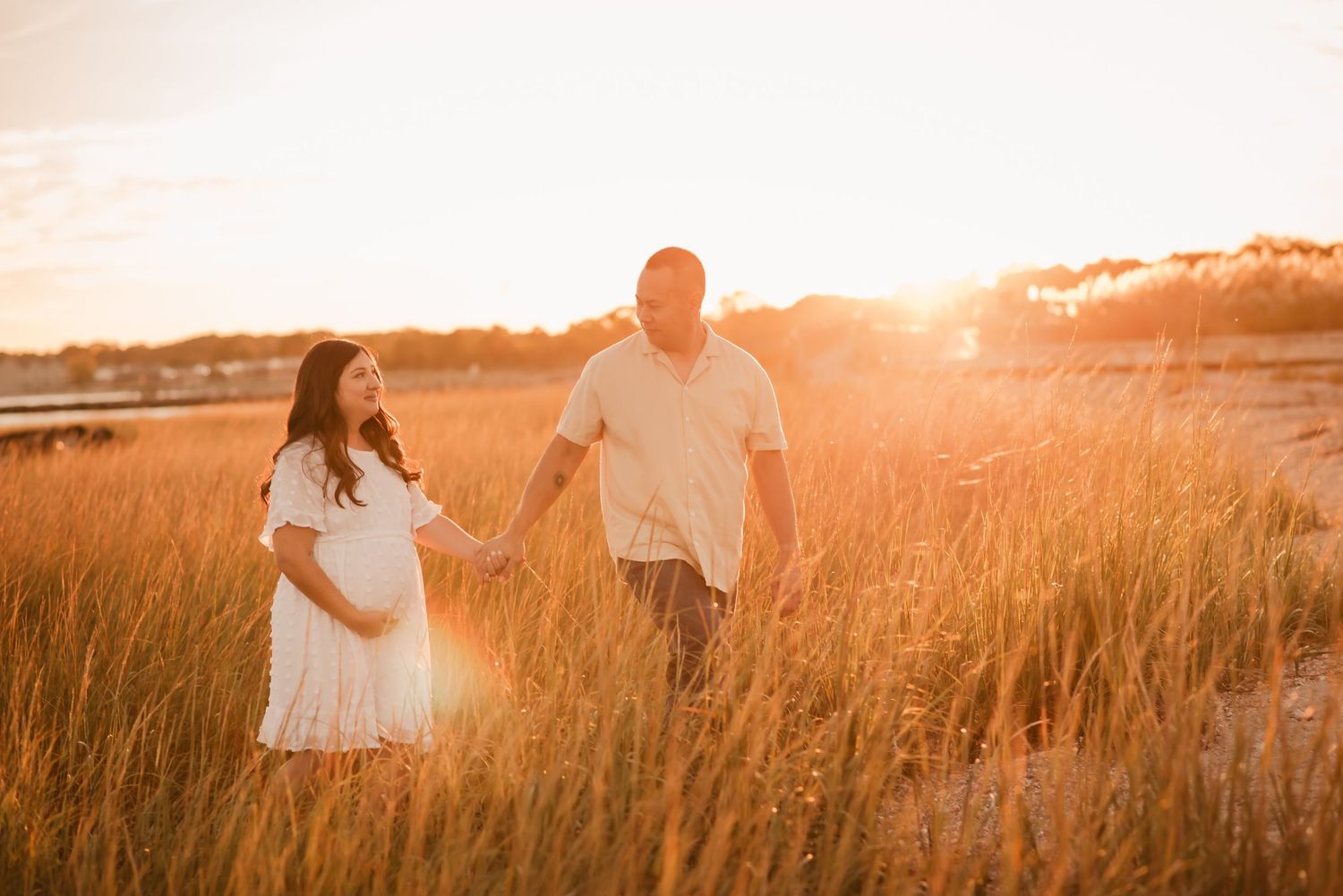 Two people holding hands in a golden field at sunset with warm sunlight glowing through tall grass.