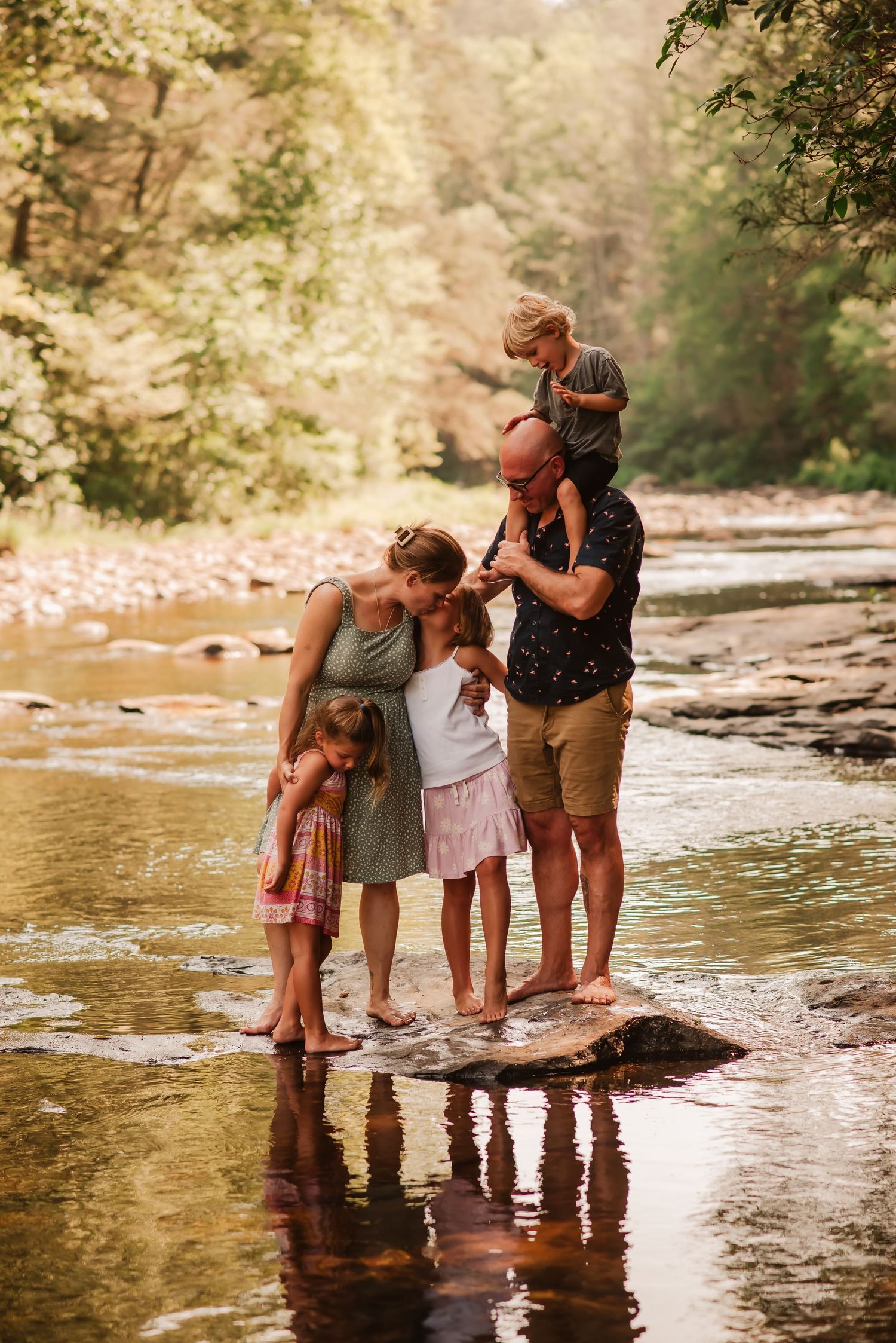Family enjoying a summer day wading in a shallow creek with sunlight filtering through trees in the background.