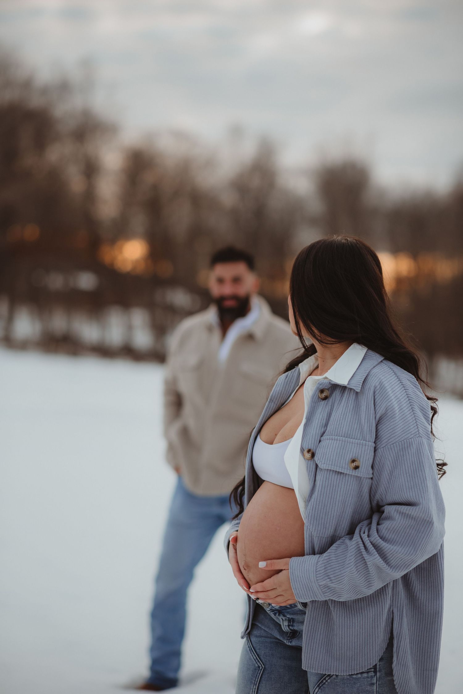 A couple embraces in a snowy winter landscape at sunset wearing casual denim and light jackets.