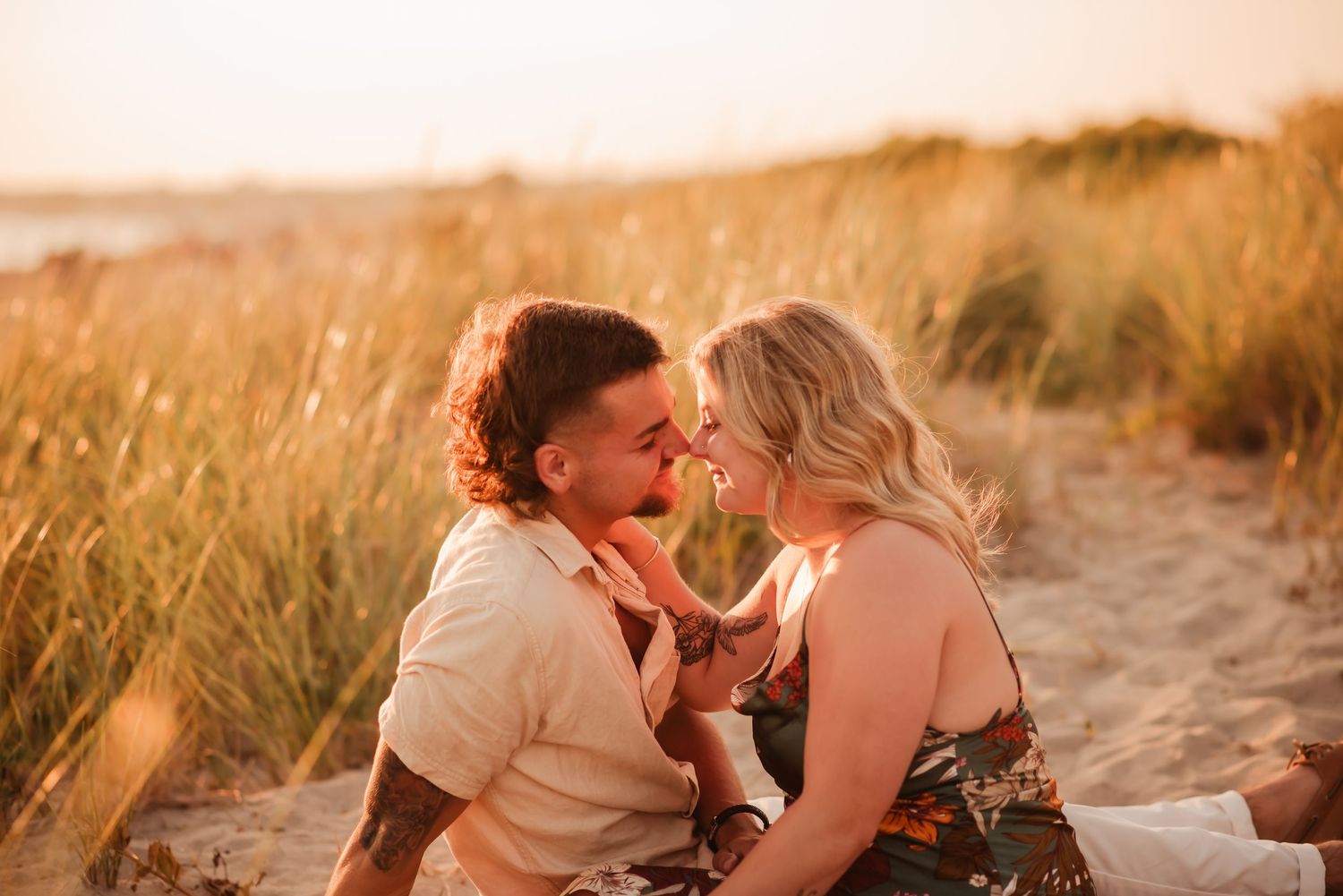 A couple shares tender moments in a golden field at sunset while being photographed in a romantic lifestyle session.