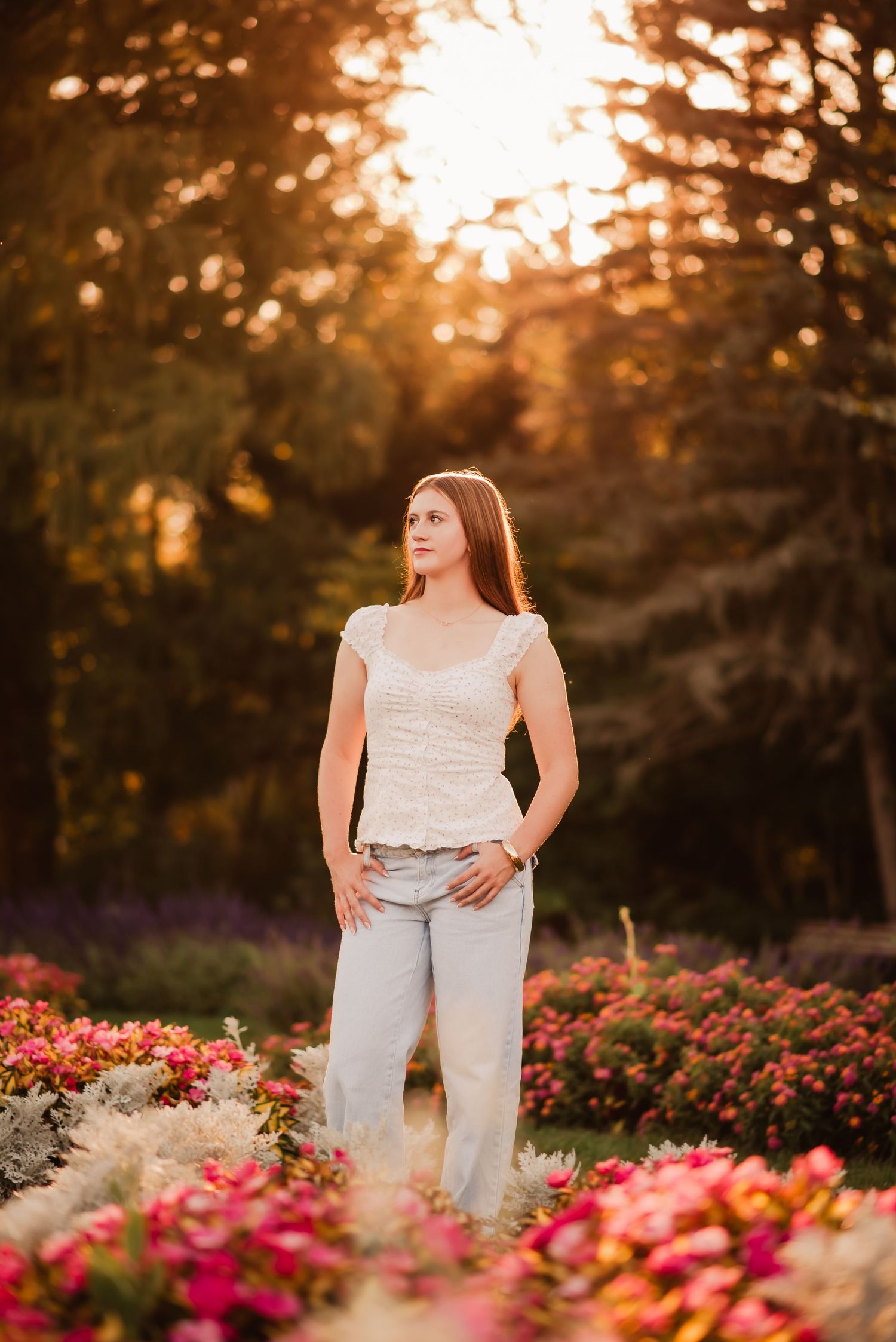 A person in white stands among vibrant pink flowers during golden sunset hour in a garden setting.
