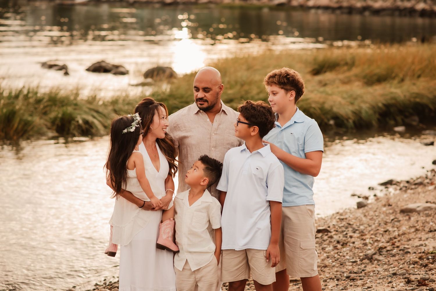 Family enjoying a sunset photoshoot on a rocky beach shore wearing coordinated neutral colored outfits.