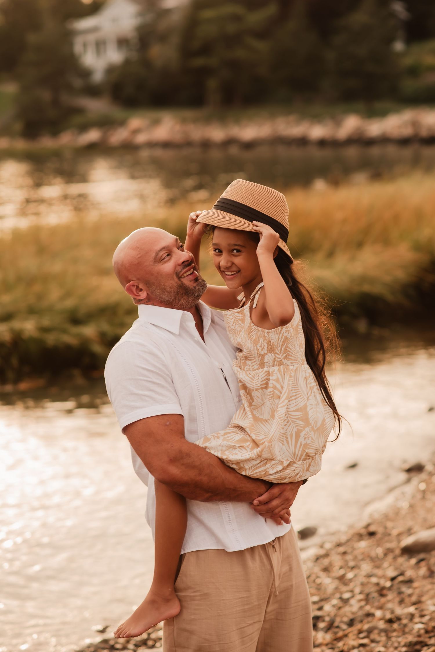 A couple embraces on a scenic beach at sunset, sharing intimate moments in matching white and beige outfits.