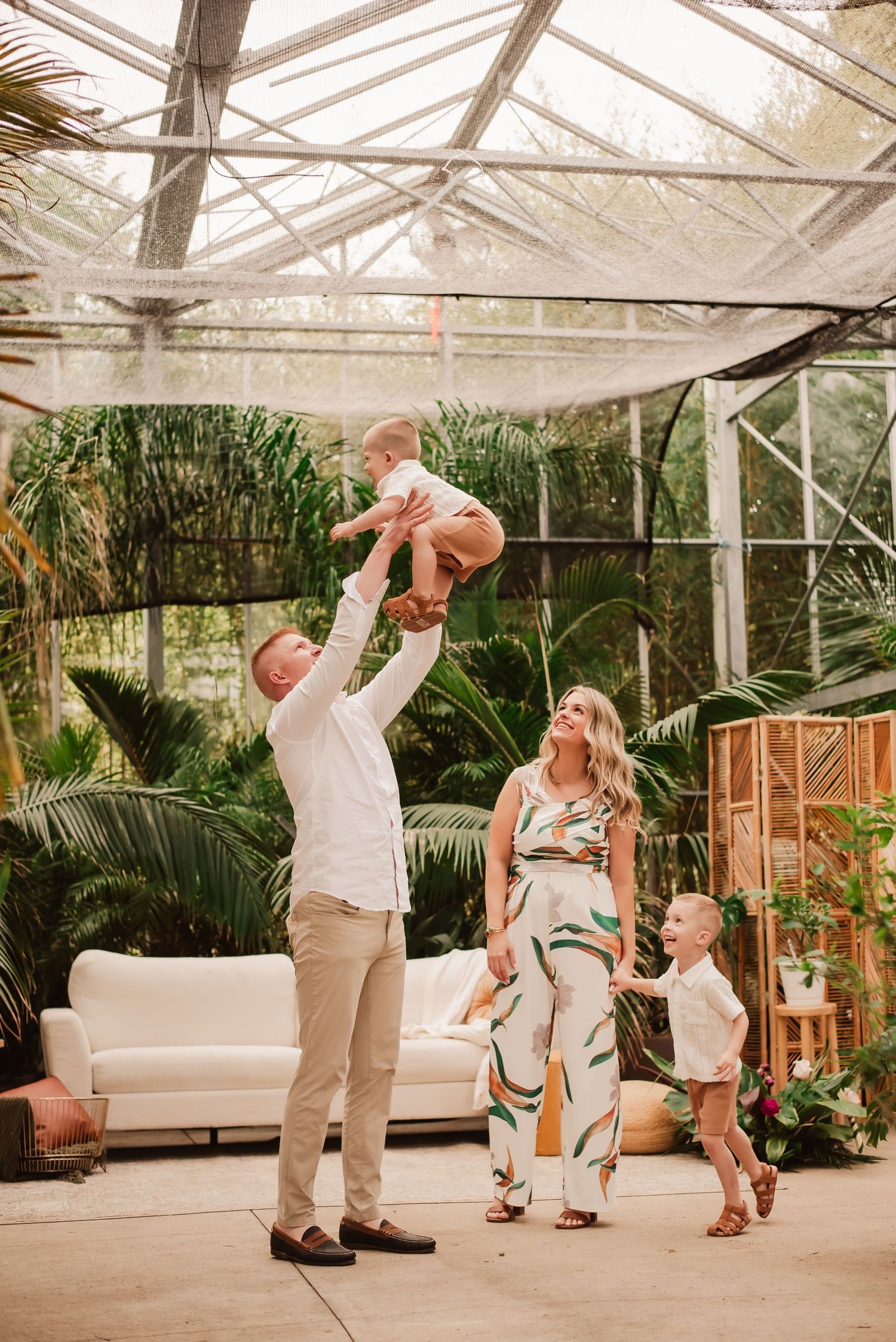 Family enjoying a tender moment together in a greenhouse with tropical plants and modern furniture.