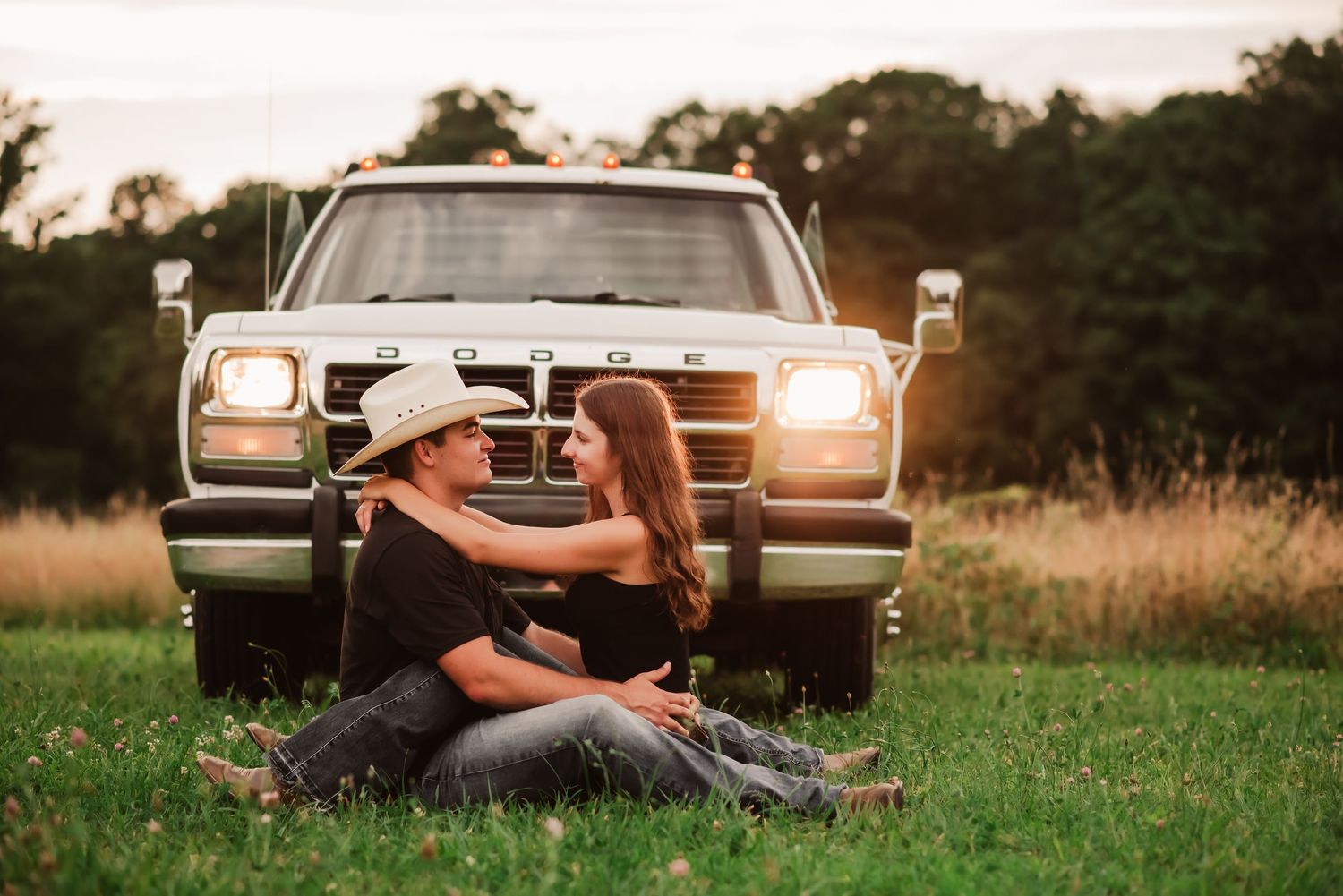 Couple relaxing in back of pickup truck at sunset in grassy field with romantic golden light.