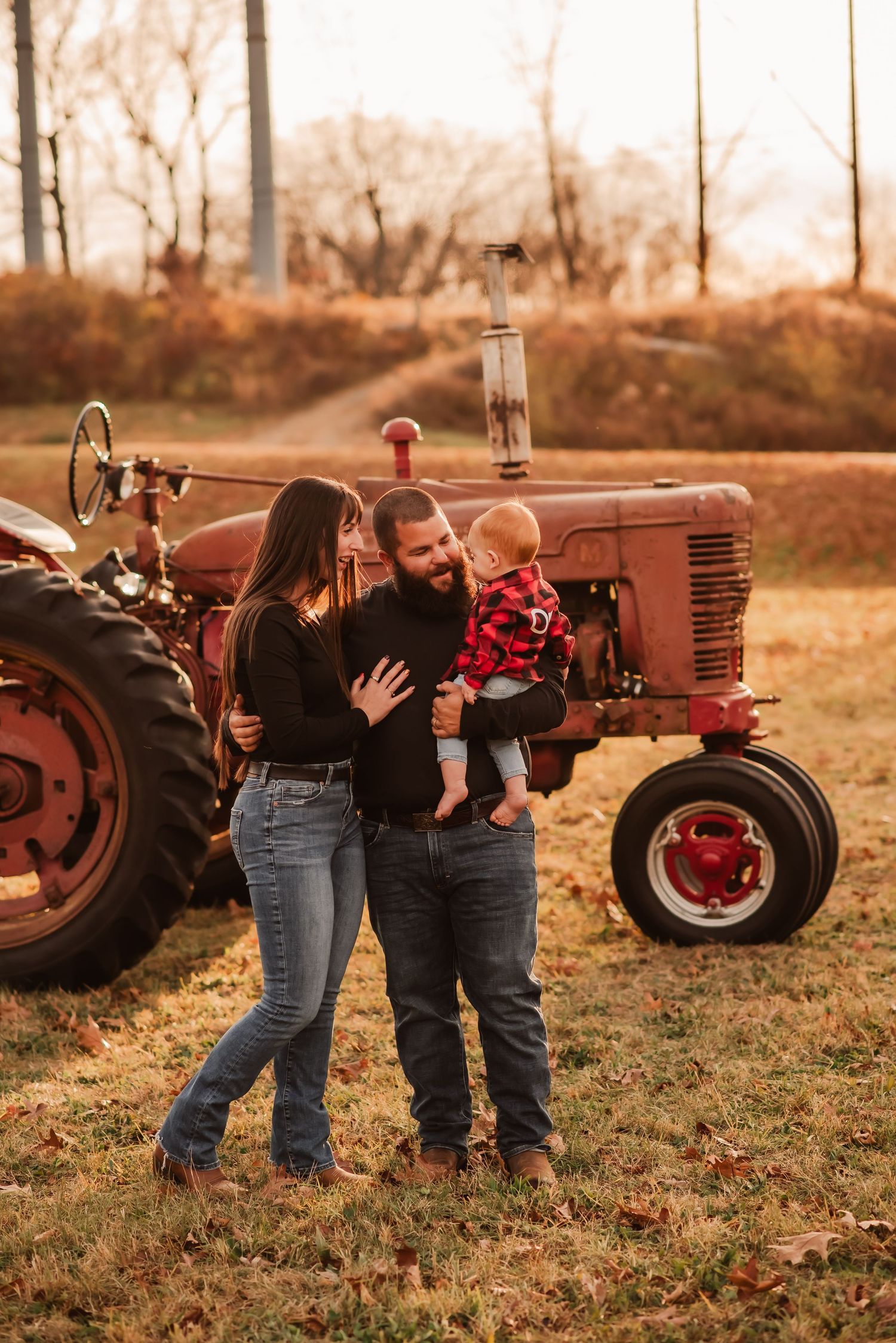 Couple sharing a romantic moment in front of vintage red tractors during a rustic autumn photoshoot.