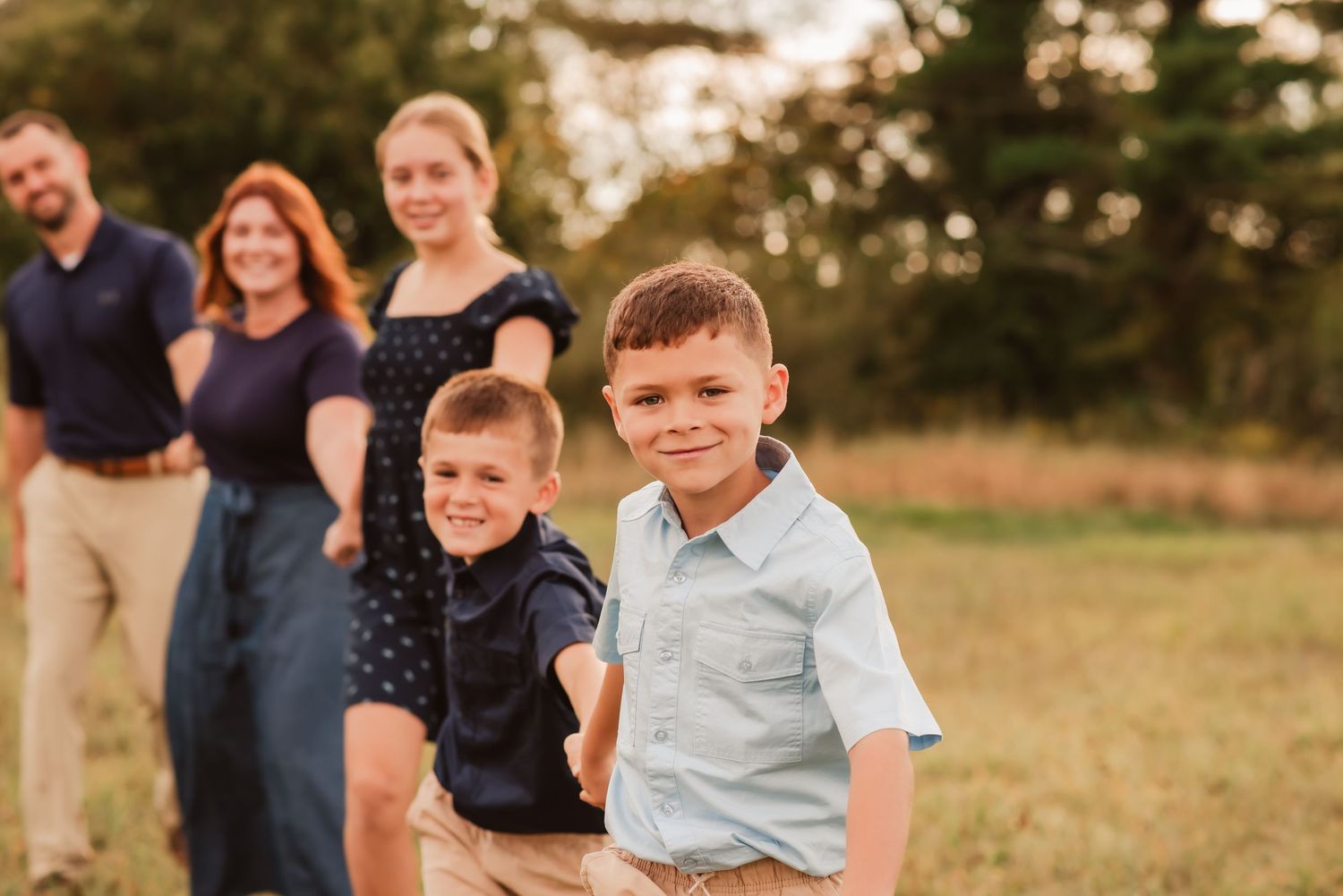 Family poses together in a grassy field at sunset during an outdoor portrait session.