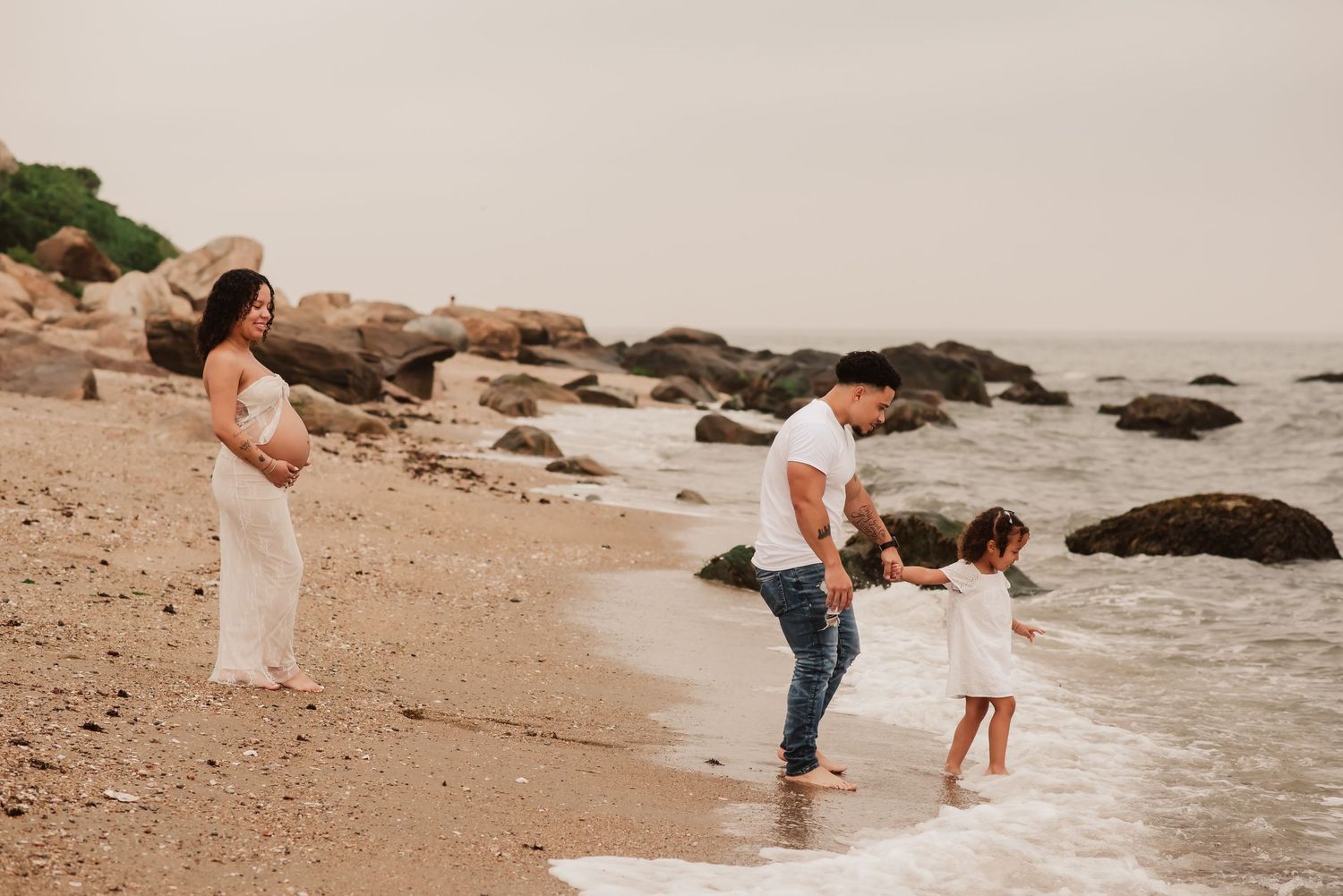 Family enjoying a peaceful moment together at a rocky beach during sunset as waves lap at their feet.