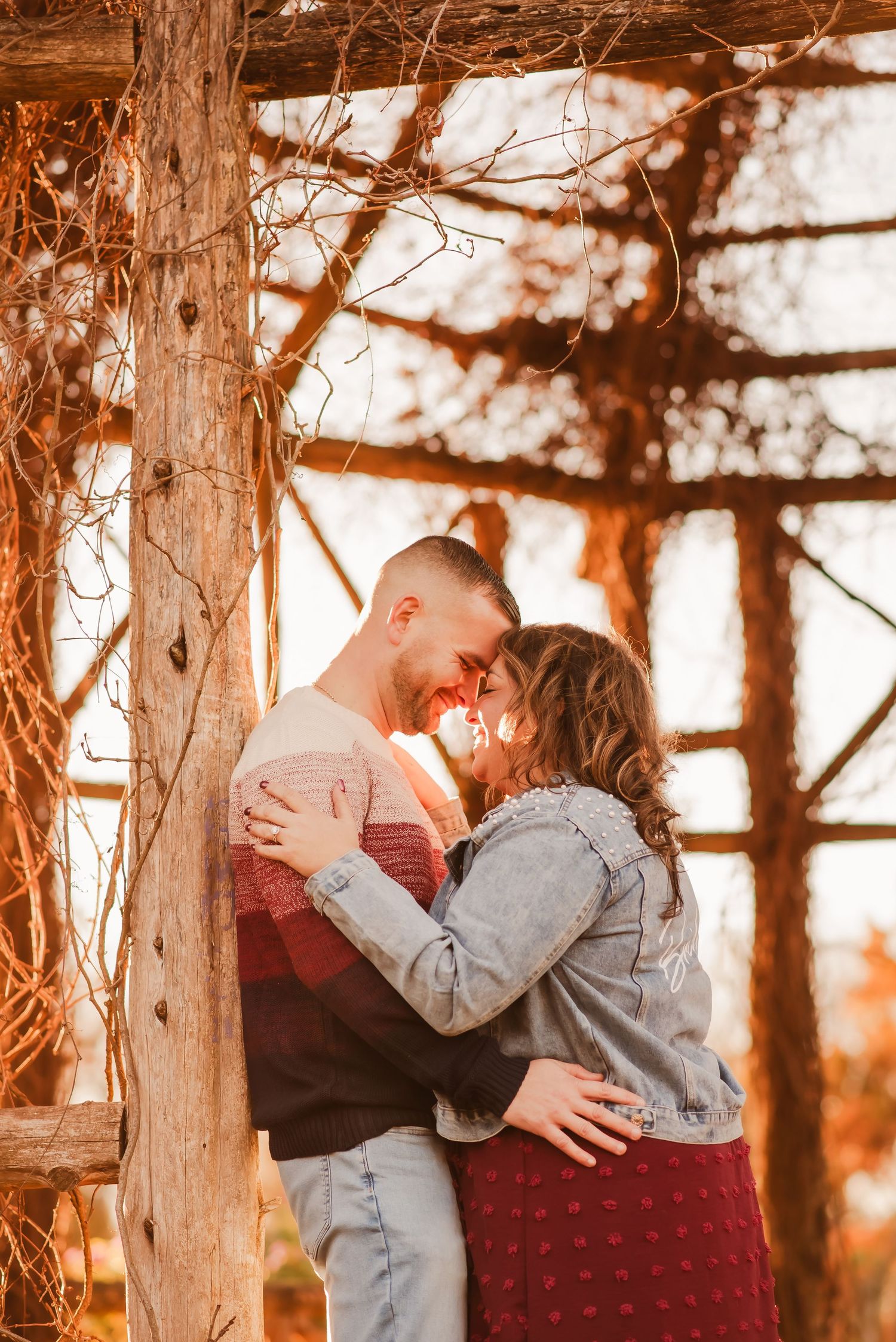 A couple embraces in a rustic wooden gazebo during golden hour sunset, creating a romantic silhouette.