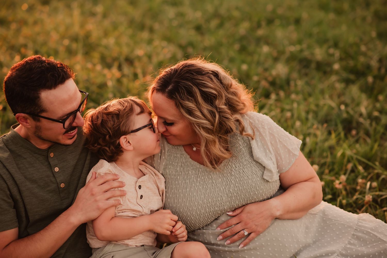 A couple shares an intimate moment outdoors during a golden hour photoshoot in a grassy field.