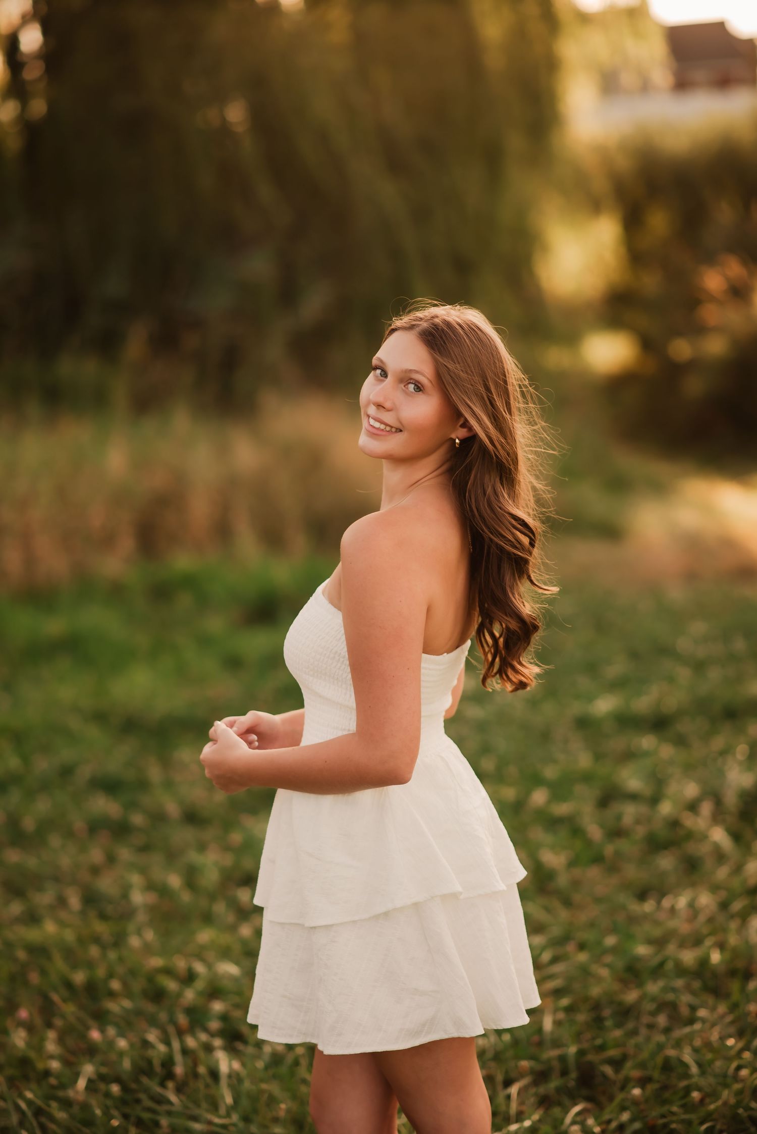 A person in a white sundress twirls playfully in a sunlit meadow during golden hour.