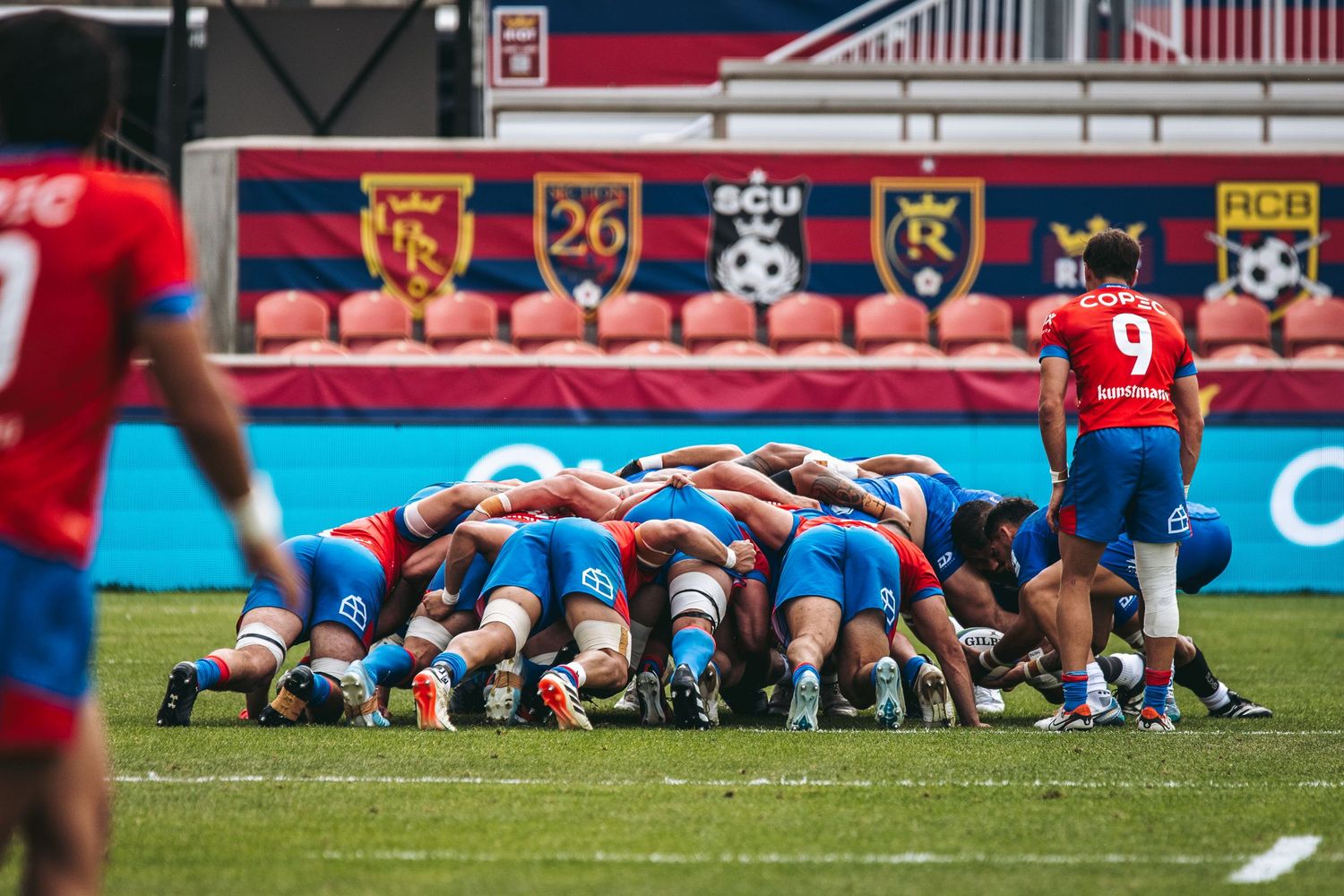 Rugby players from opposing teams engage in a scrum formation during a competitive match on the field.