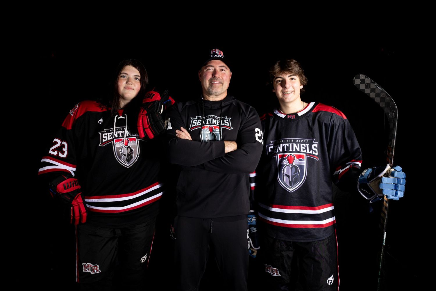 A group of hockey players pose together wearing black and red jerseys in a dark setting.