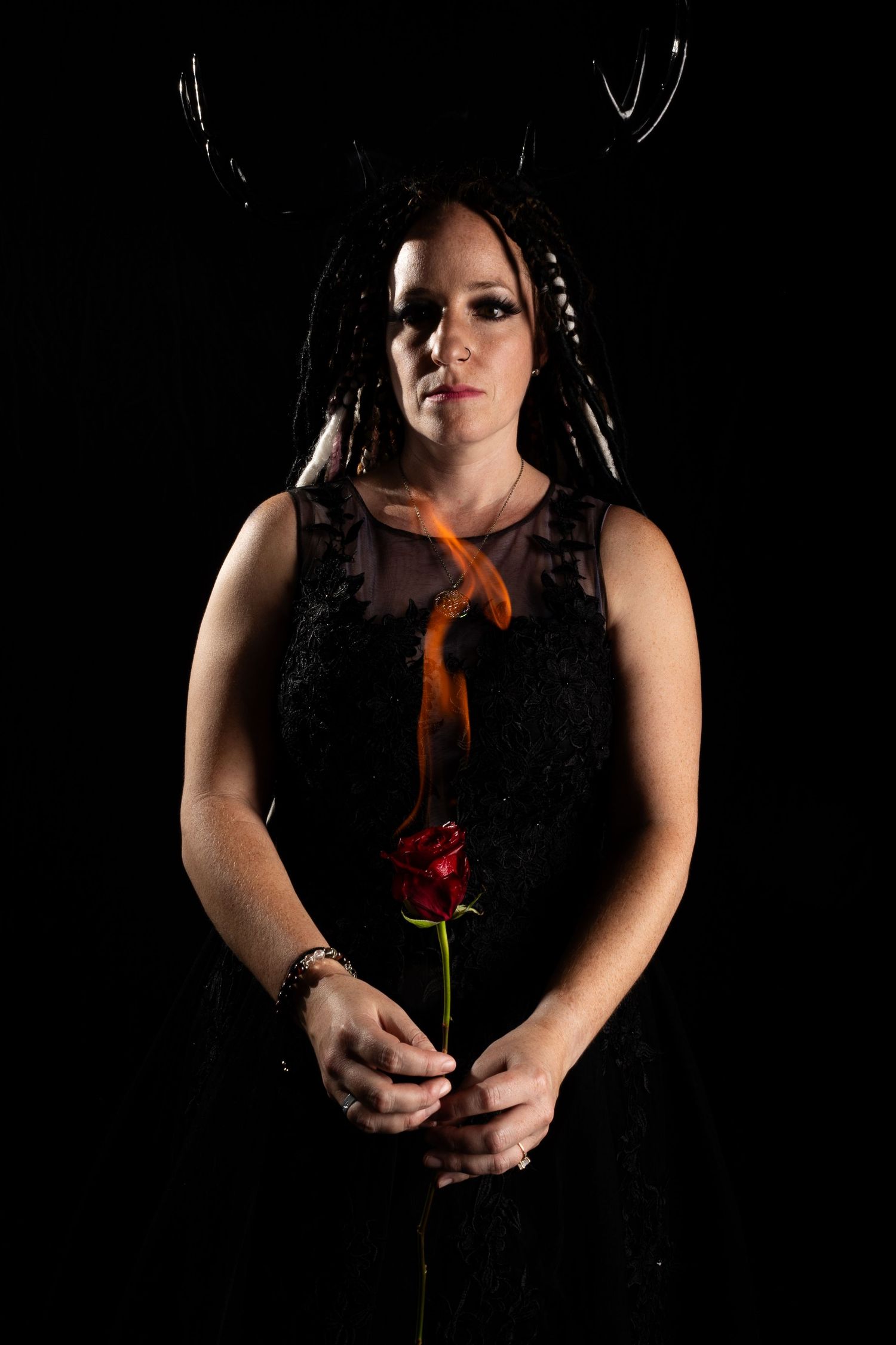 Person in black holding burning flower against dark background.