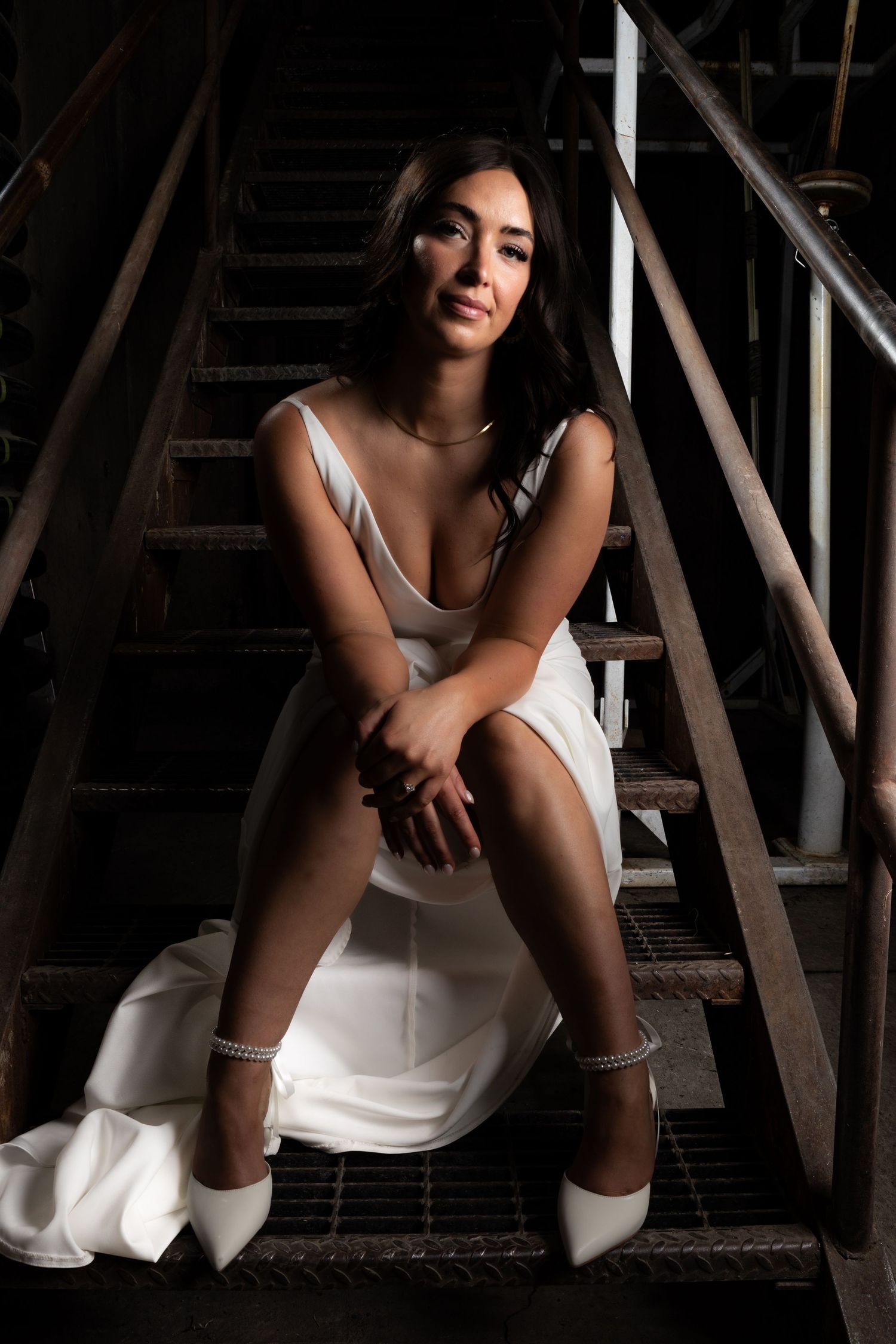 Figure in white dress sitting on wooden stairs in dramatic lighting.