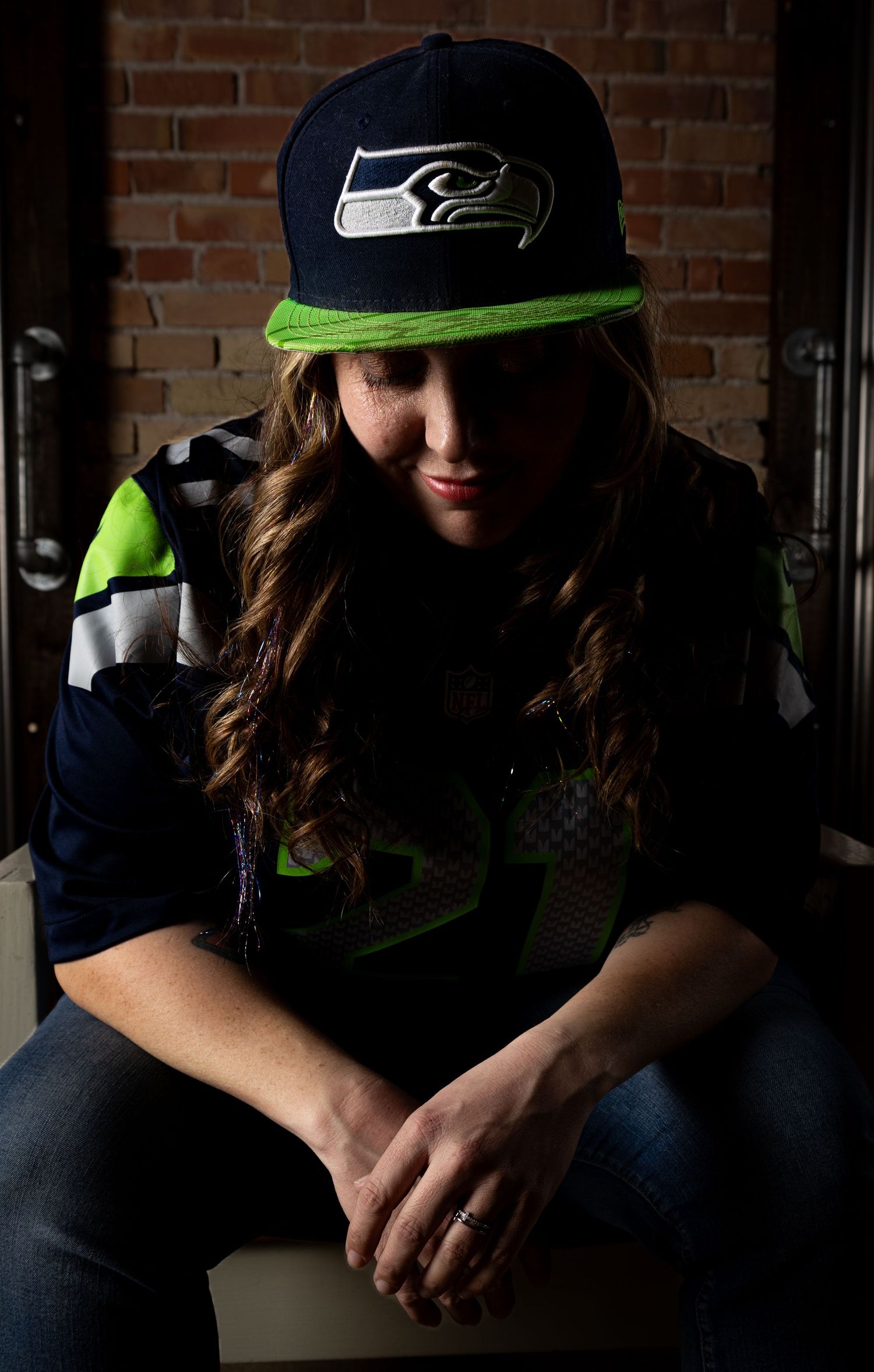 Seattle Seahawks fan wearing team cap and jersey in moody lighting against brick wall.