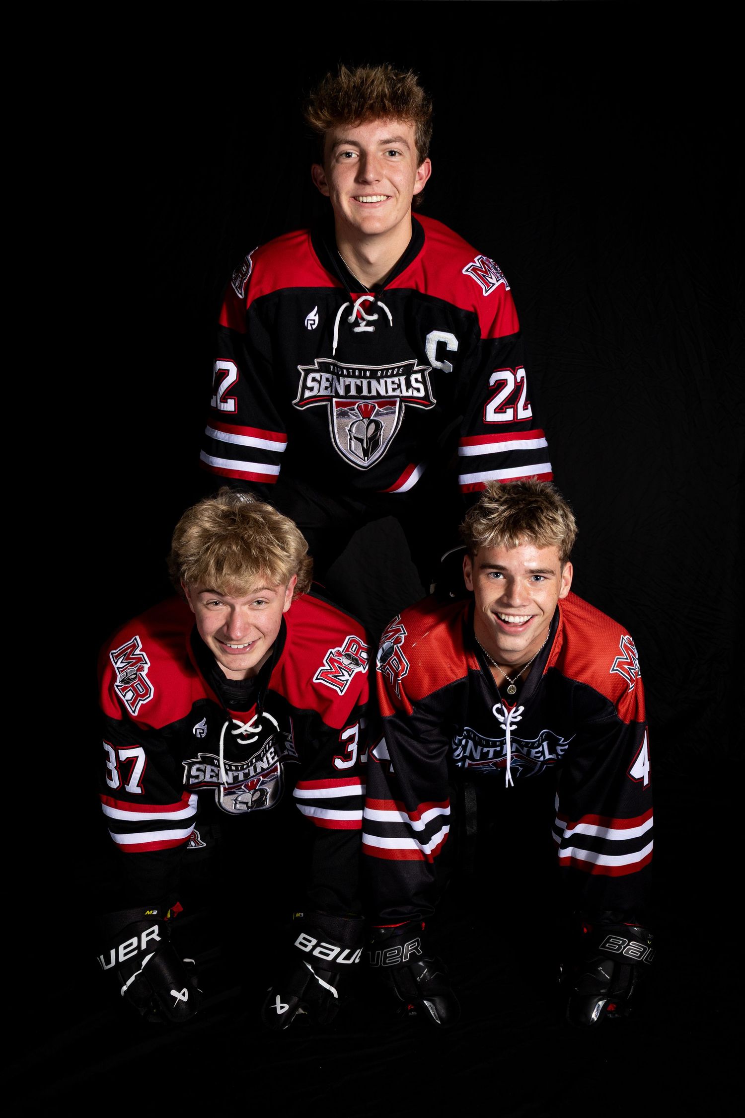 Hockey players pose in black and red uniforms against dark background for team photos.