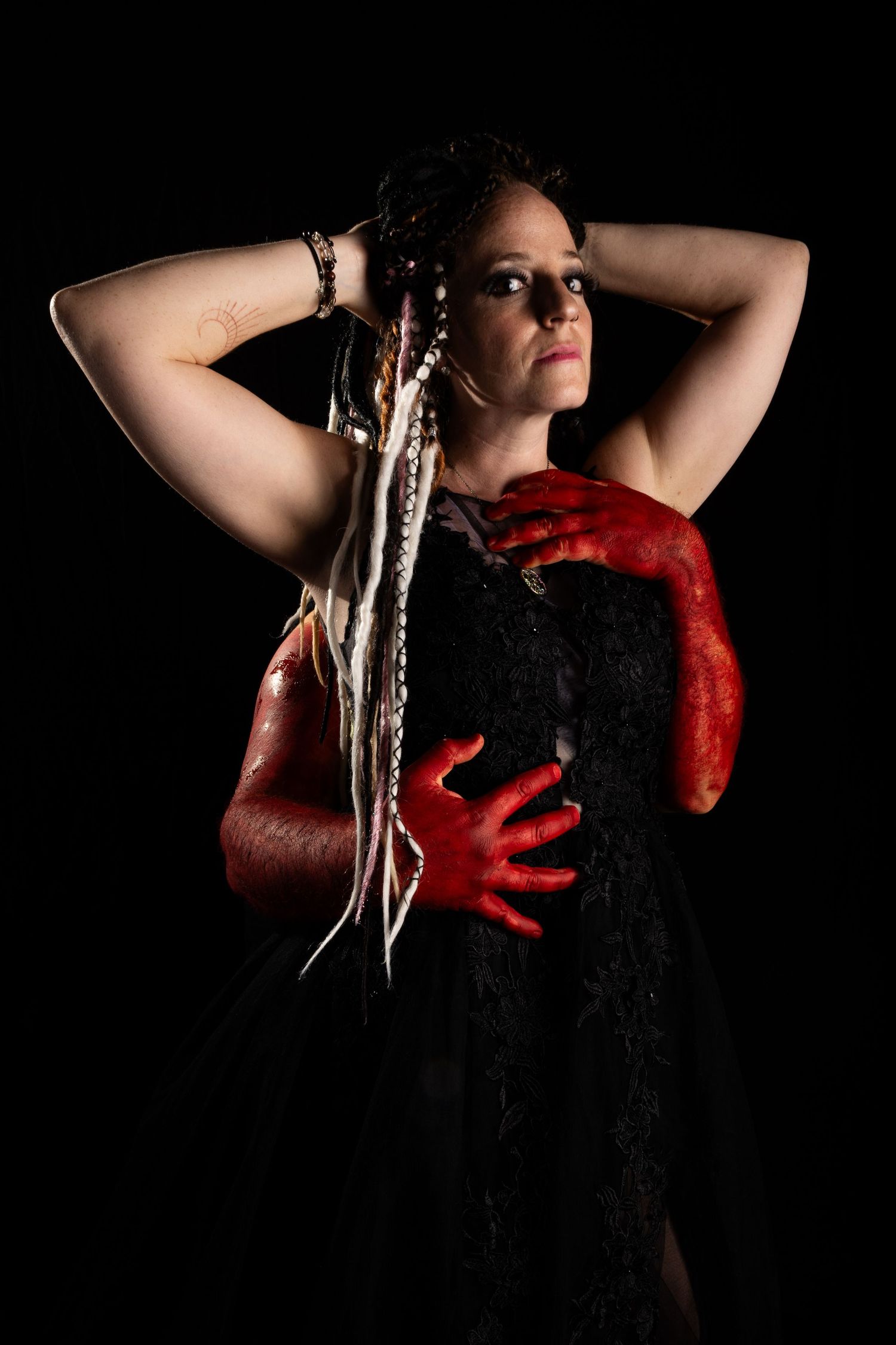 Figure in black dress with red gloves in dramatic lighting.