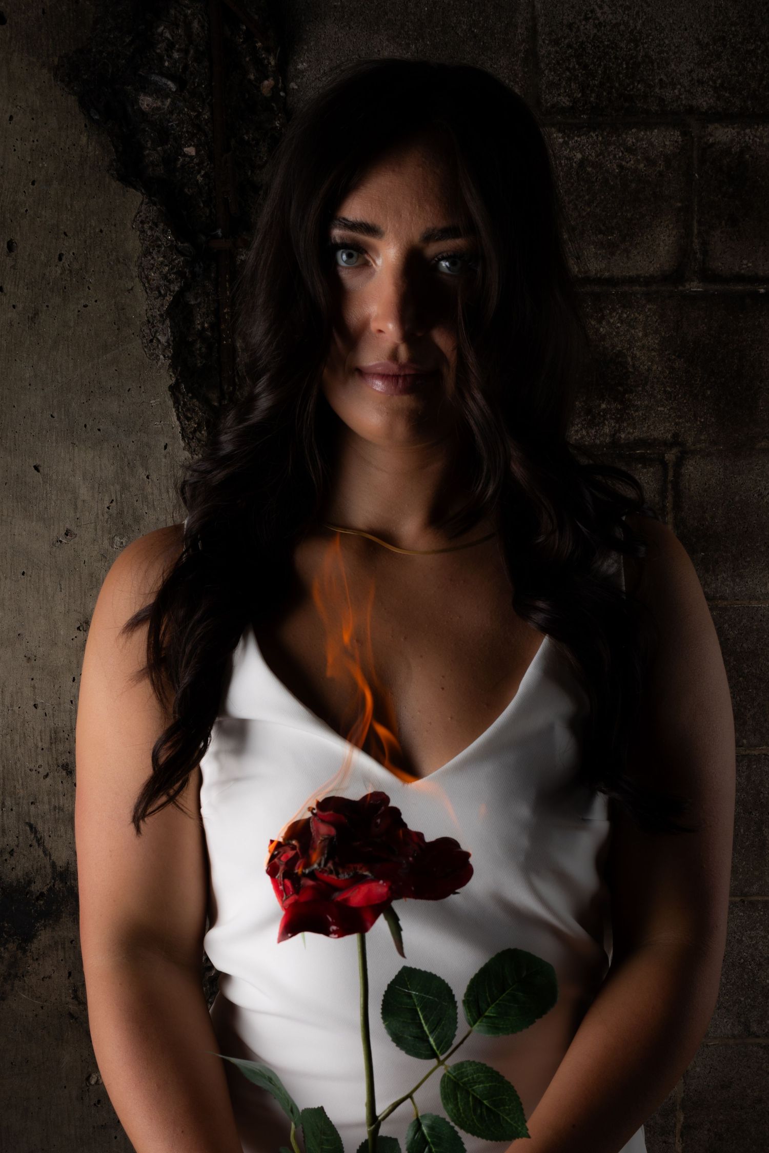 Person in white dress holding burning rose against concrete wall.