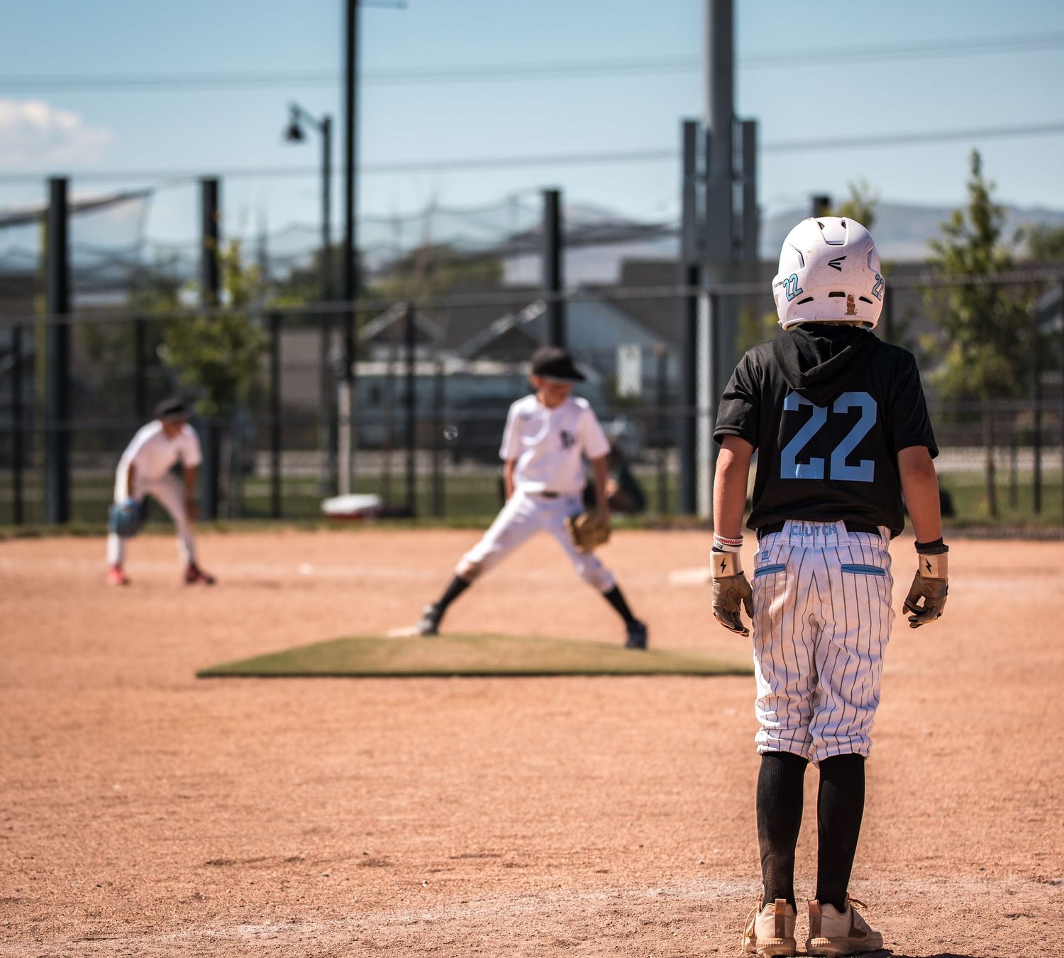 Baseball players in white uniforms stand on a dusty infield during a sunny game on a baseball diamond.
