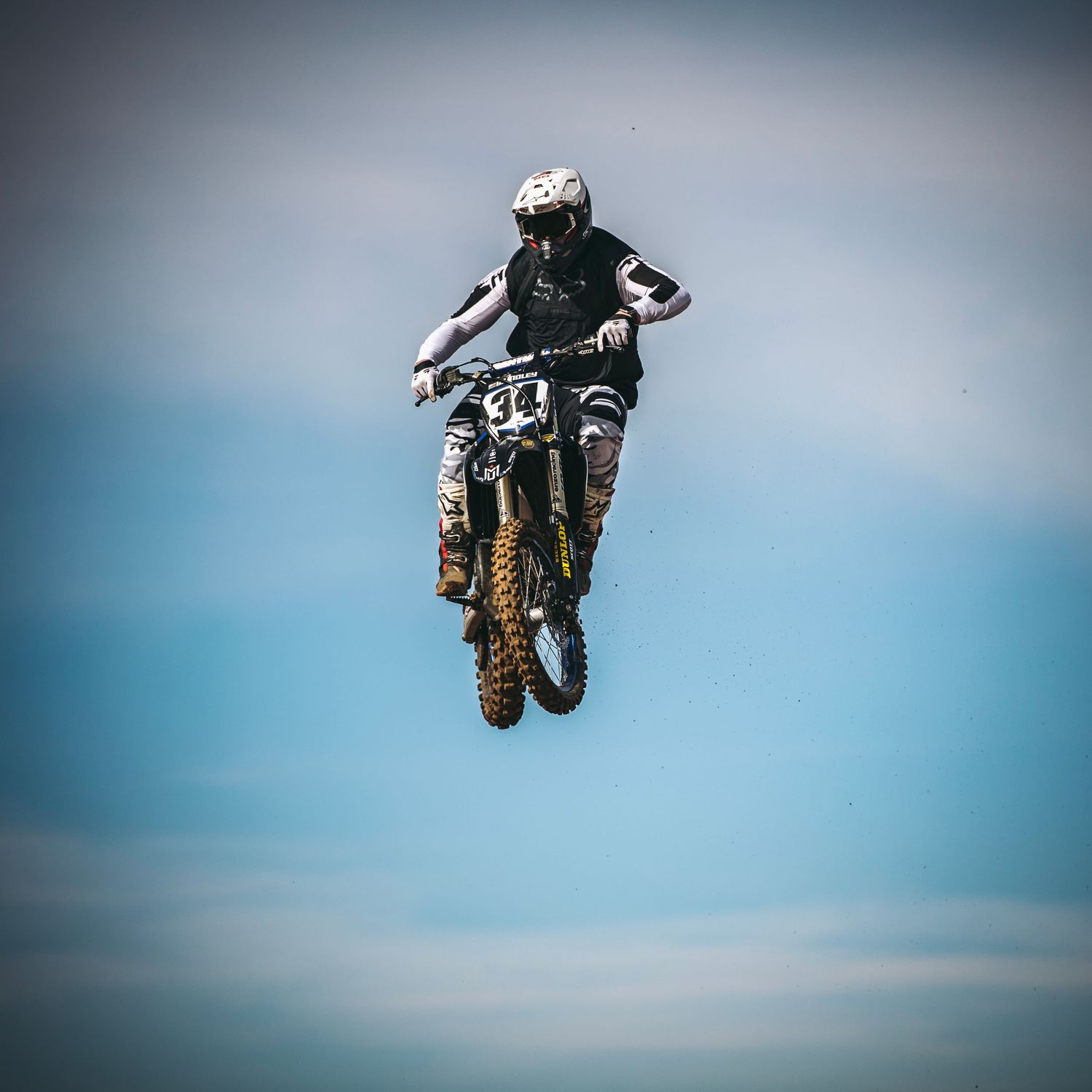 Motocross rider performing aerial stunt against blue sky during freestyle jump competition.