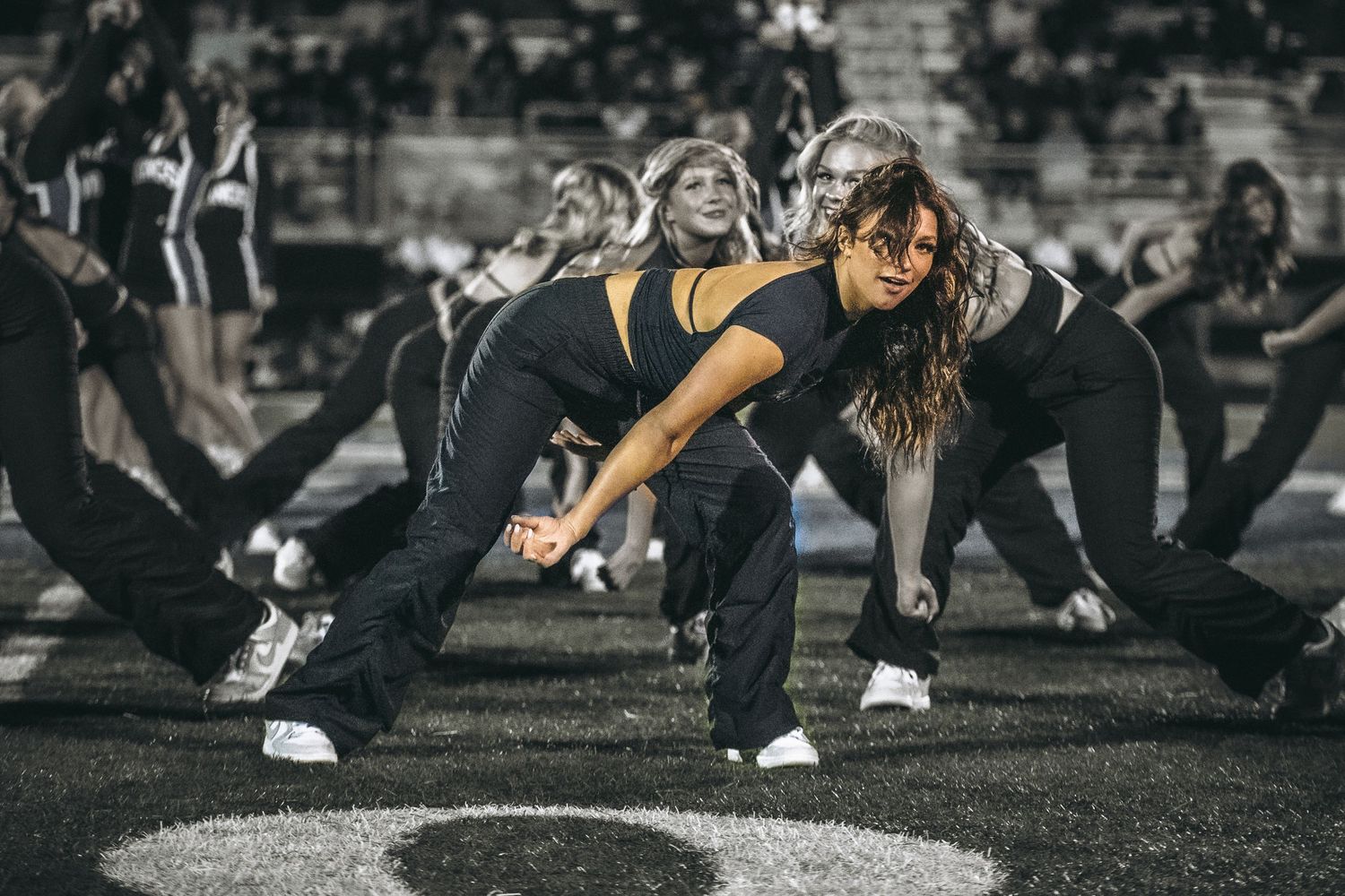 Group of dancers performing energetic hip-hop choreography on a dark field in athletic wear and sneakers.