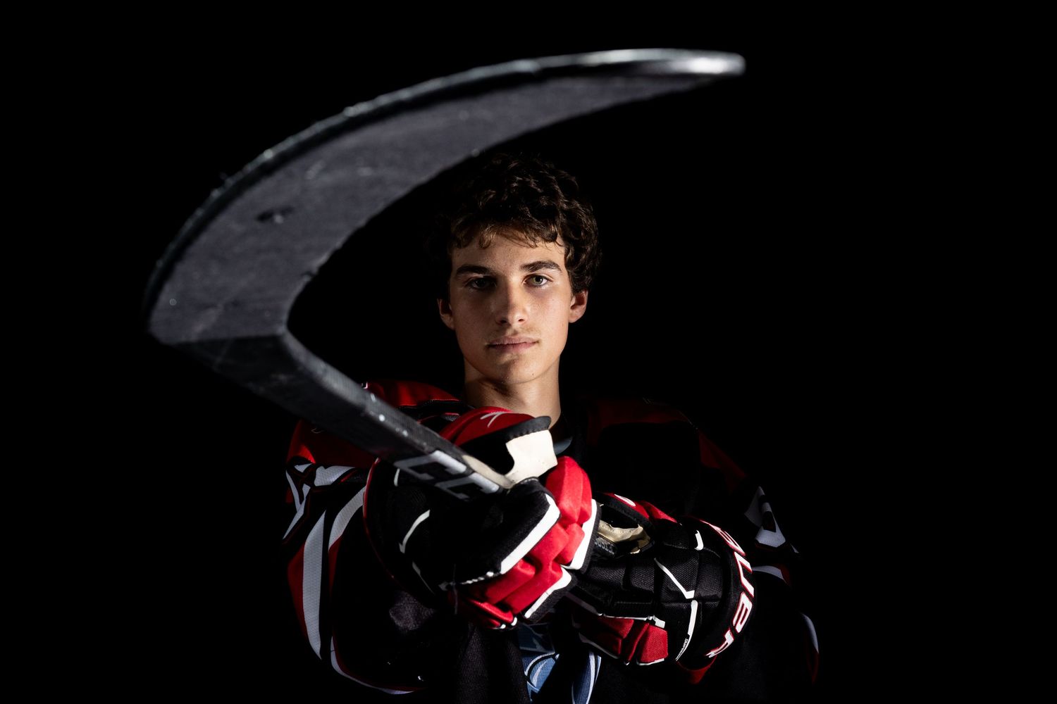 A hockey player poses dramatically in dark lighting while holding their stick against a black background.