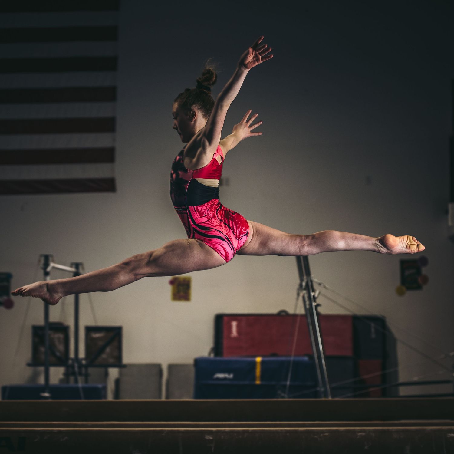 Gymnast performs a graceful split leap sequence on balance beam showing progression of movement in dark gym setting.