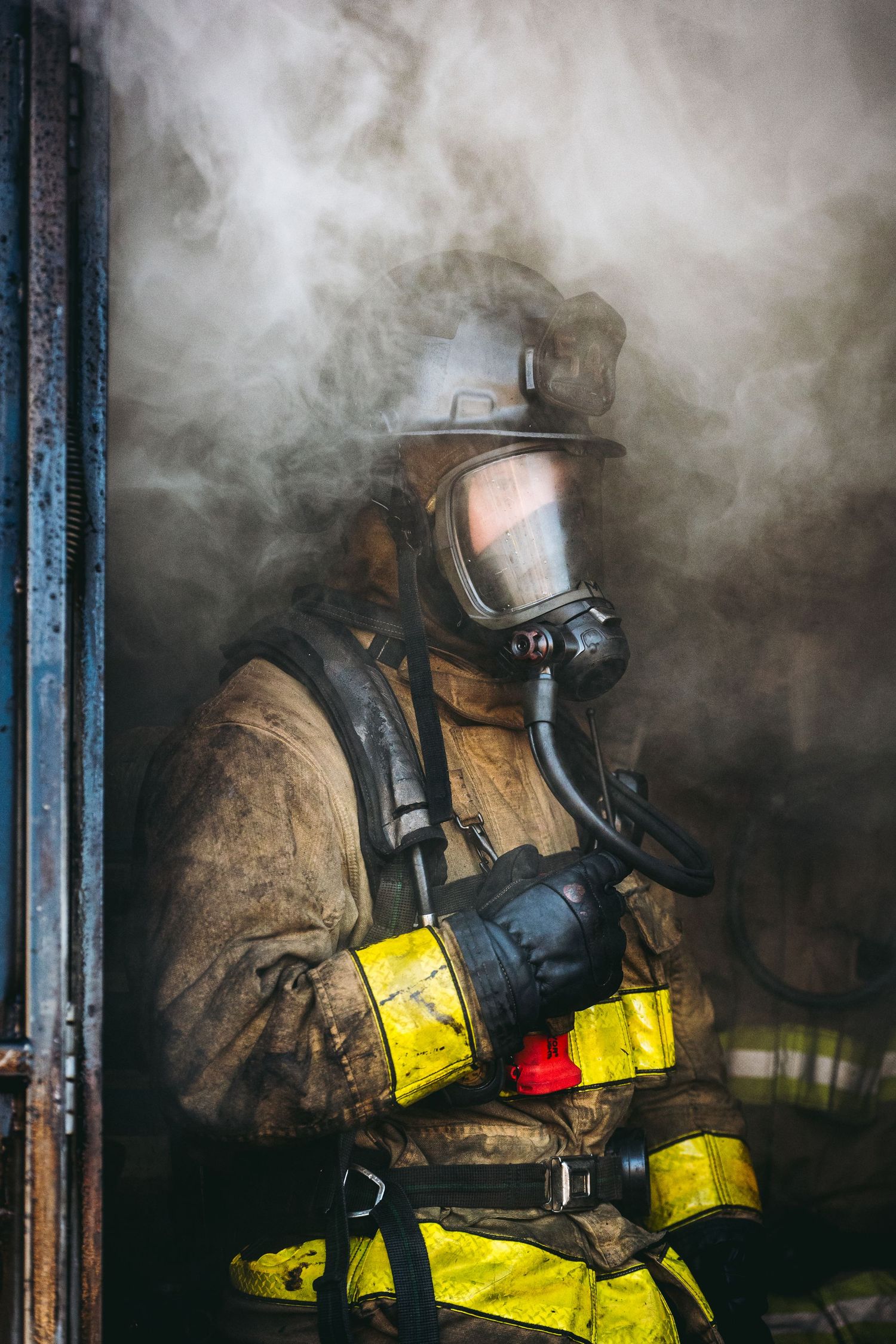 A firefighter in protective gear and breathing apparatus stands amid thick smoke during an emergency response.