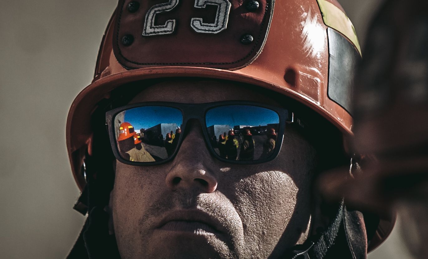 A close-up view of someone wearing a baseball helmet and reflective sunglasses with a cityscape reflection.