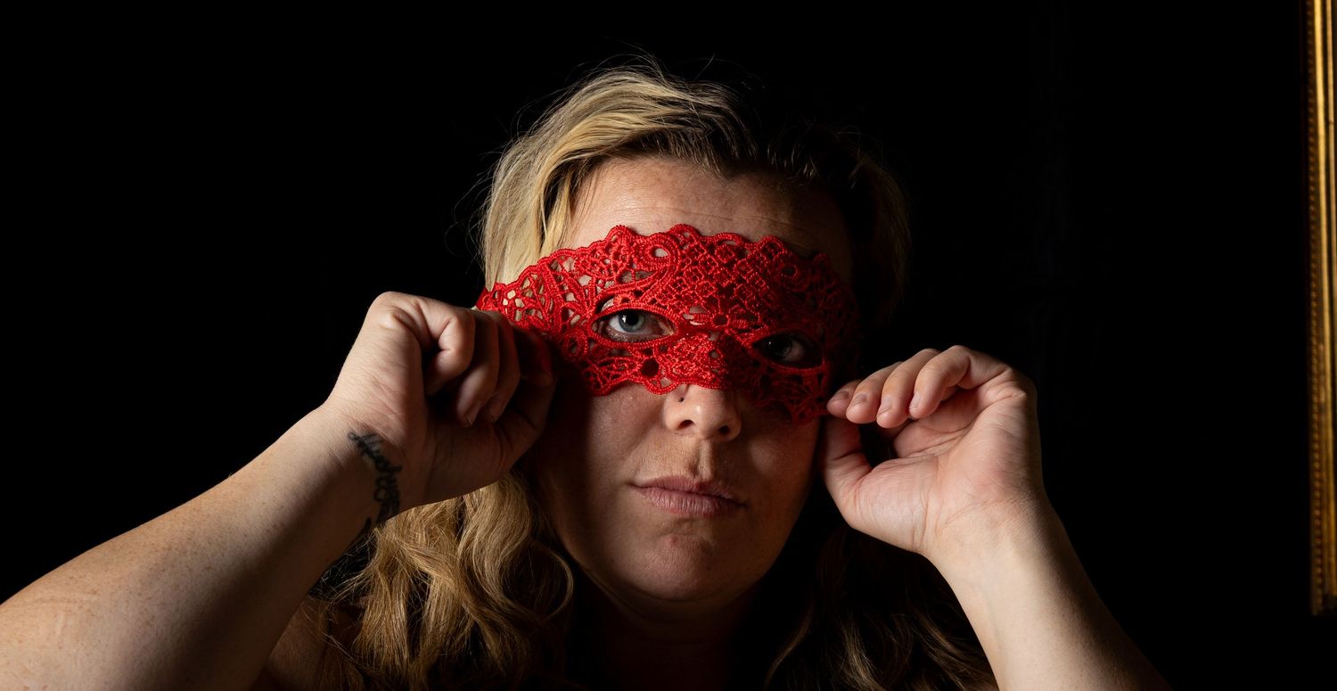 Person wearing red lace masquerade mask against dark background.