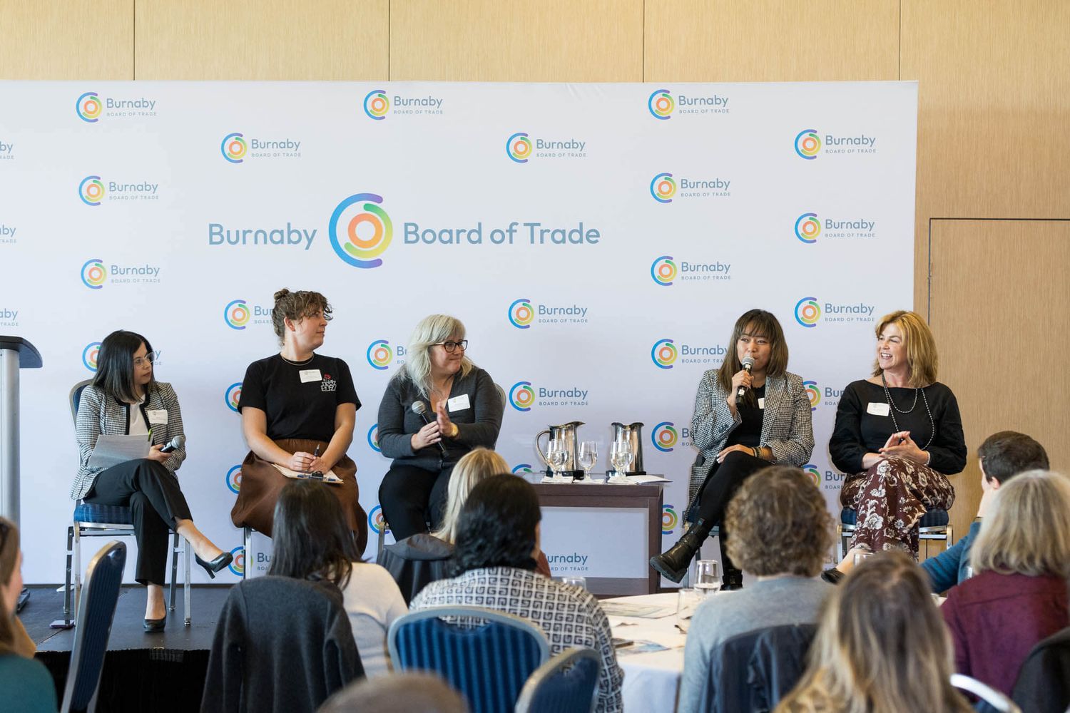 Five women panelists speak at a Burnaby Board of Trade event before an audience in a bright conference room.