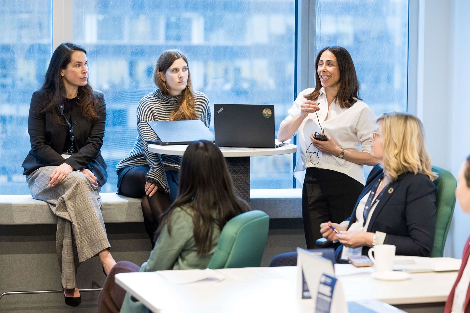 Women professionals engaged in a collaborative discussion in a modern office meeting room with large windows.