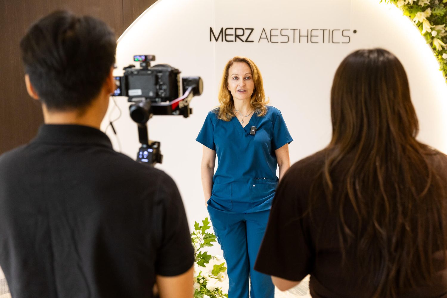 Healthcare professional in blue scrubs being filmed in front of a Merz Aesthetics branded backdrop at JW Marriott Parq Vancouver