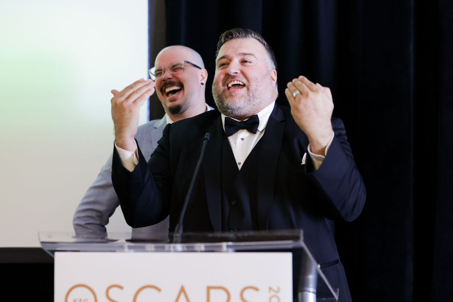 Two men in tuxedos laughing at an Oscars podium during an awards ceremony event for Keg Restaurants held at the Stanley Park Pavillion.